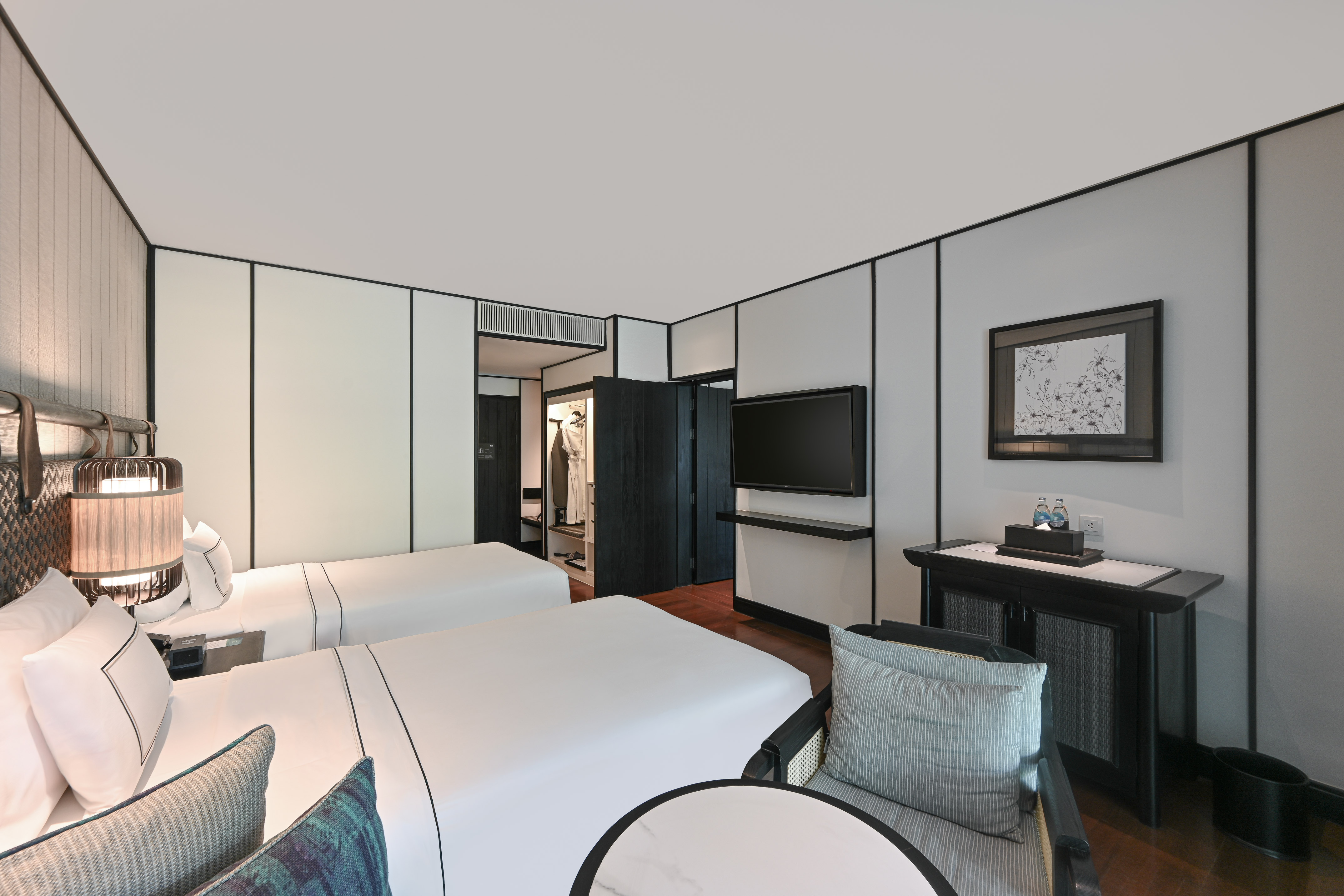 Minimalist hotel room with two twin beds, wall TV, and open wardrobe.