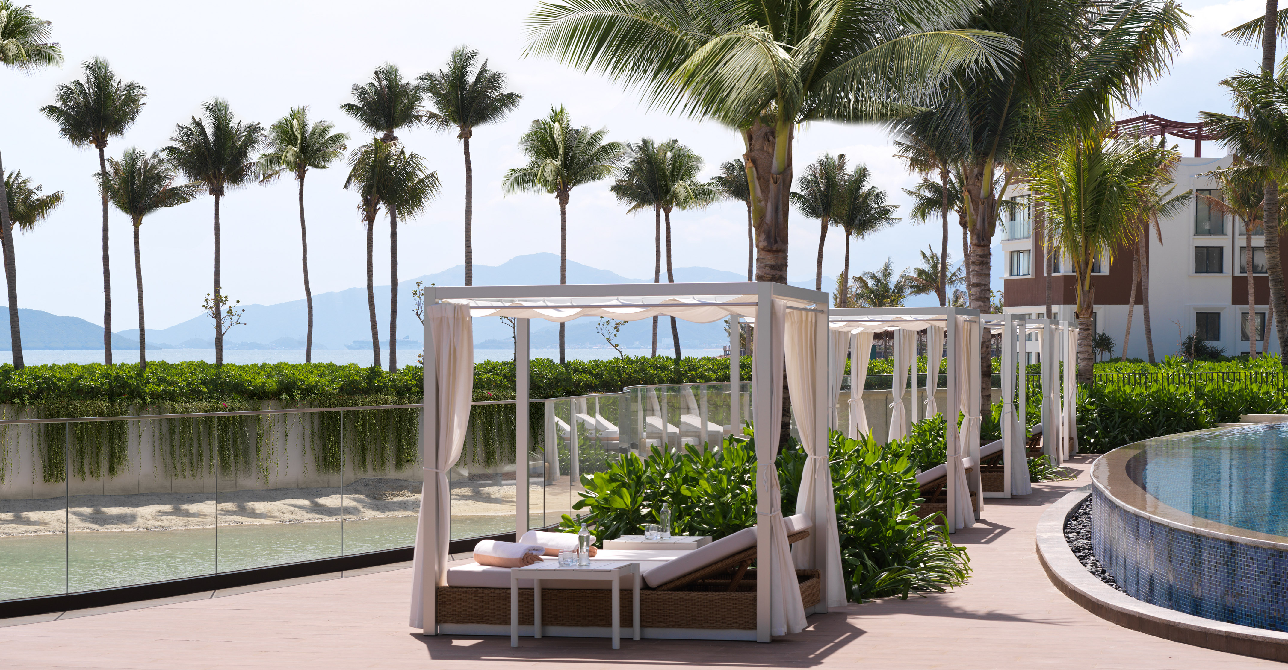 Tropical luxury resort cabanas by ocean with palm trees and pool.