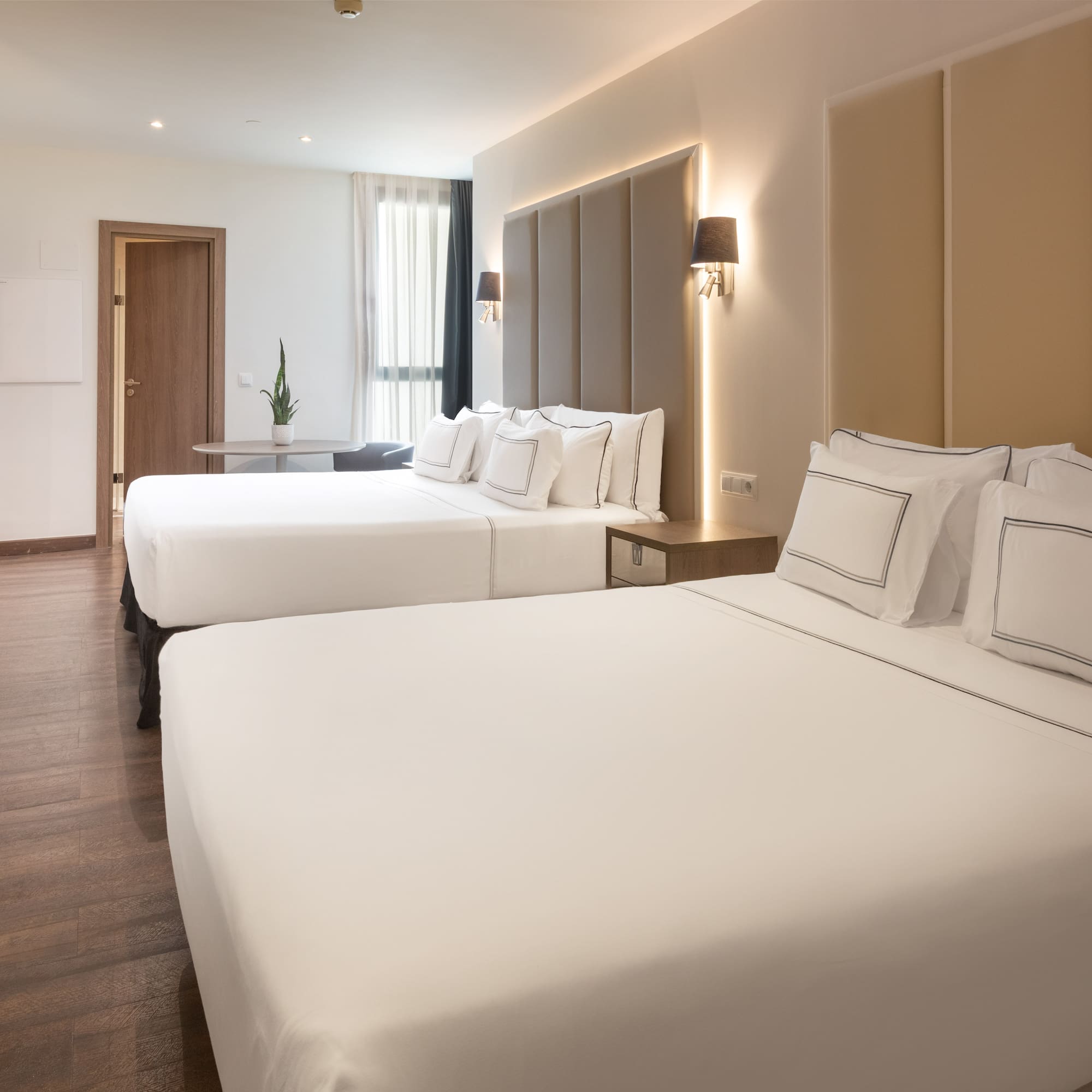 Modern hotel room with two beds, crisp white linen, and wood floor.