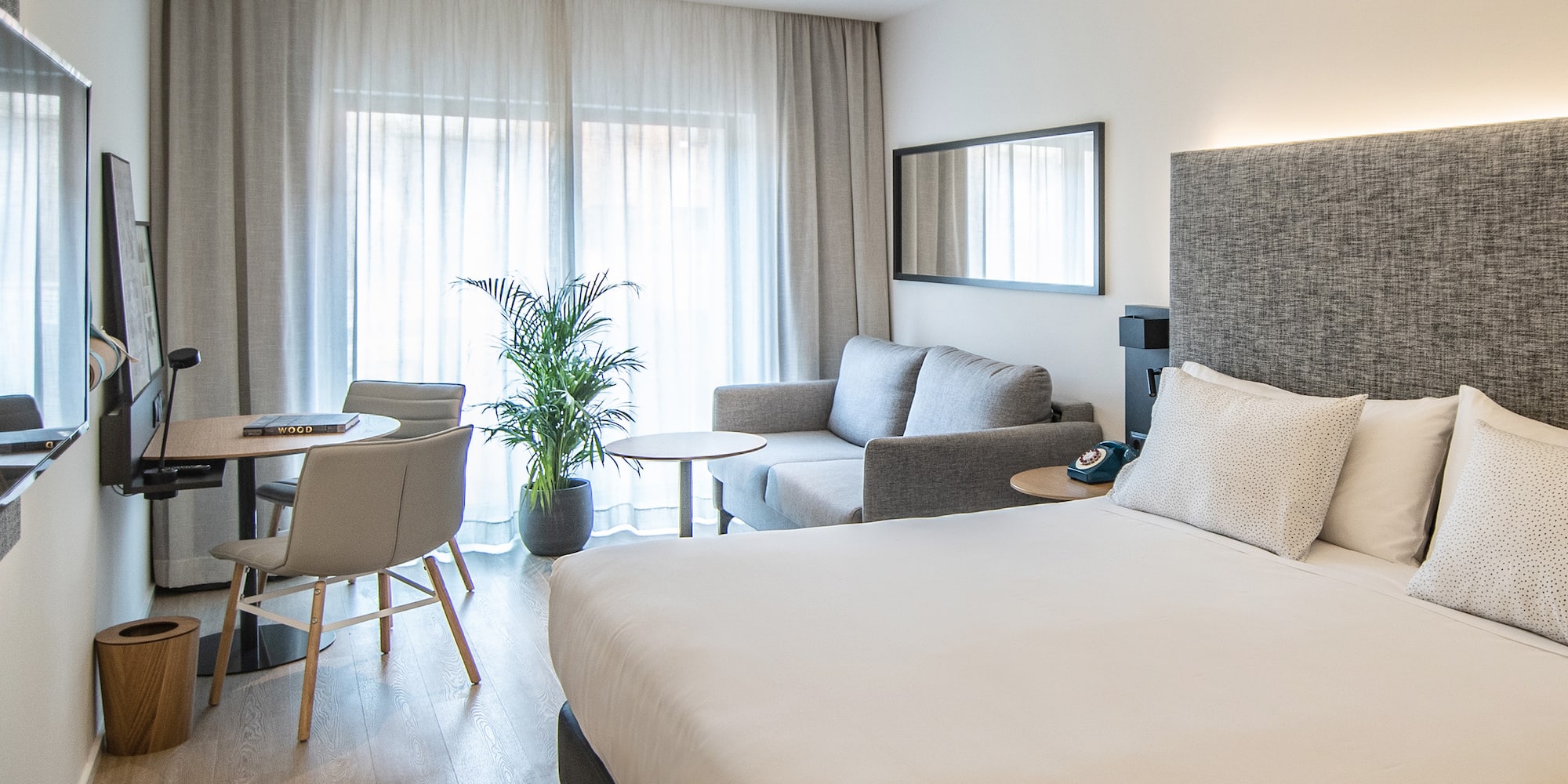 Dormitorio hotel moderno con cama, sofá, escritorio y ventanal.