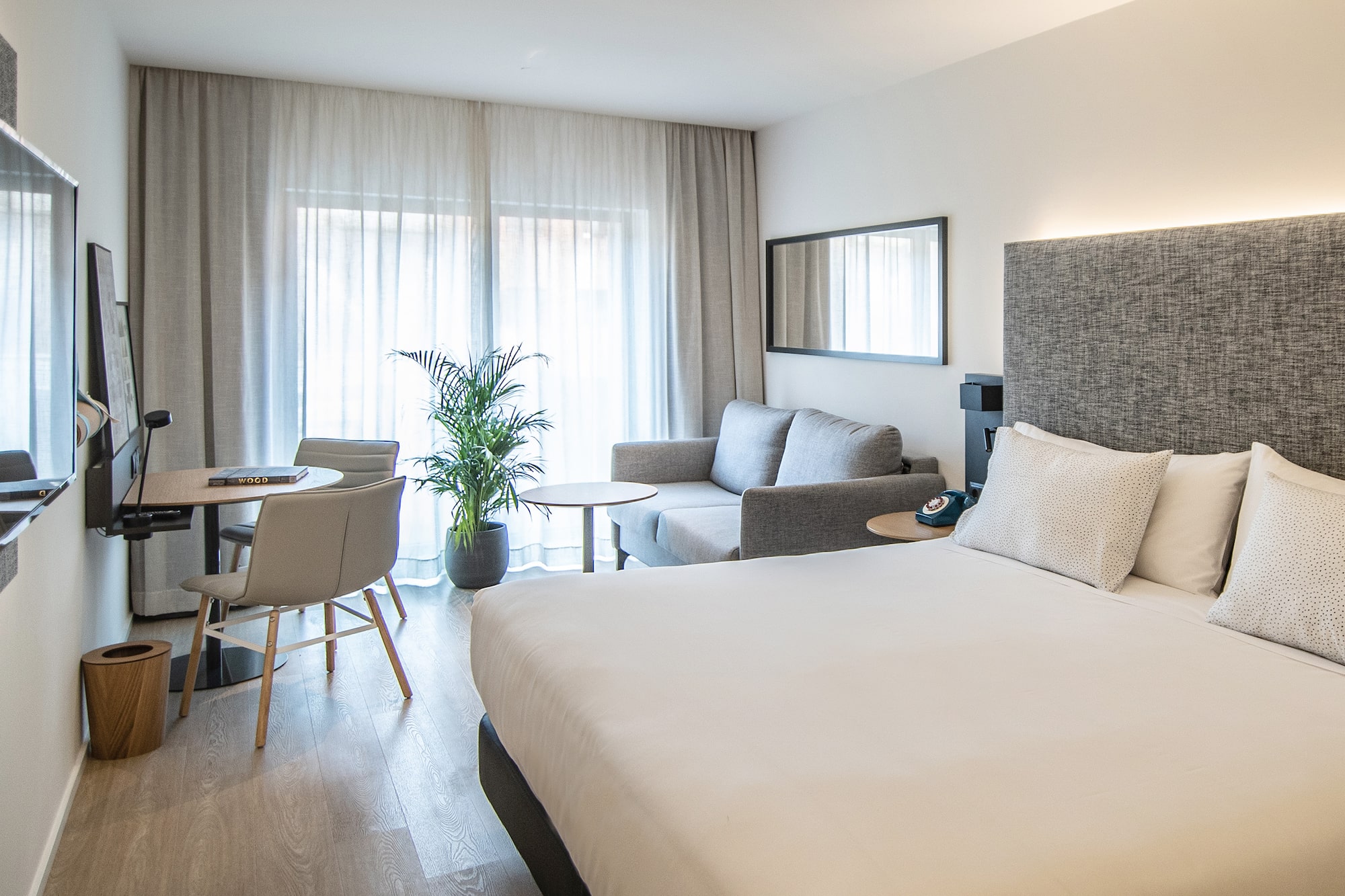 Dormitorio hotel moderno con cama, sofá, escritorio y ventanal.