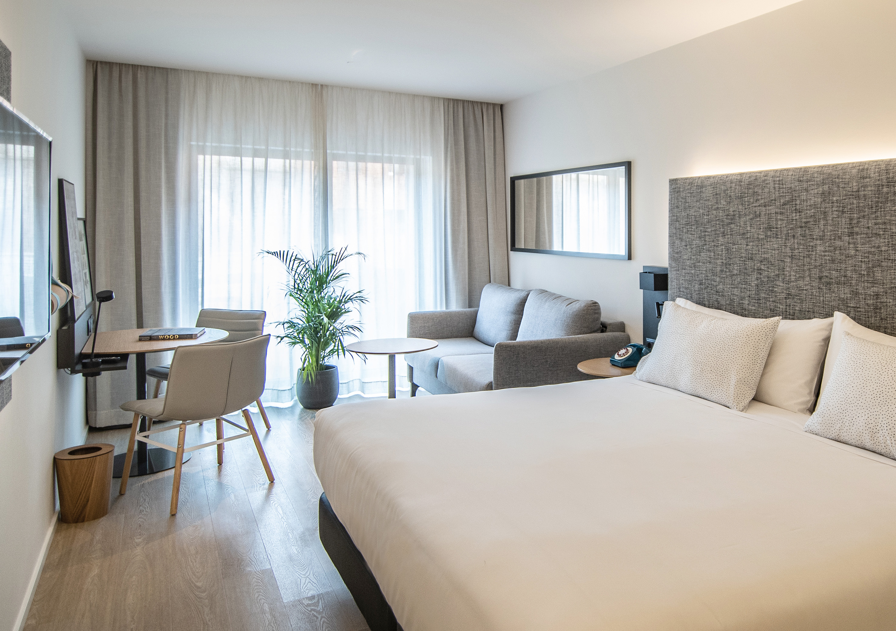 Dormitorio hotel moderno con cama, sofá, escritorio y ventanal.