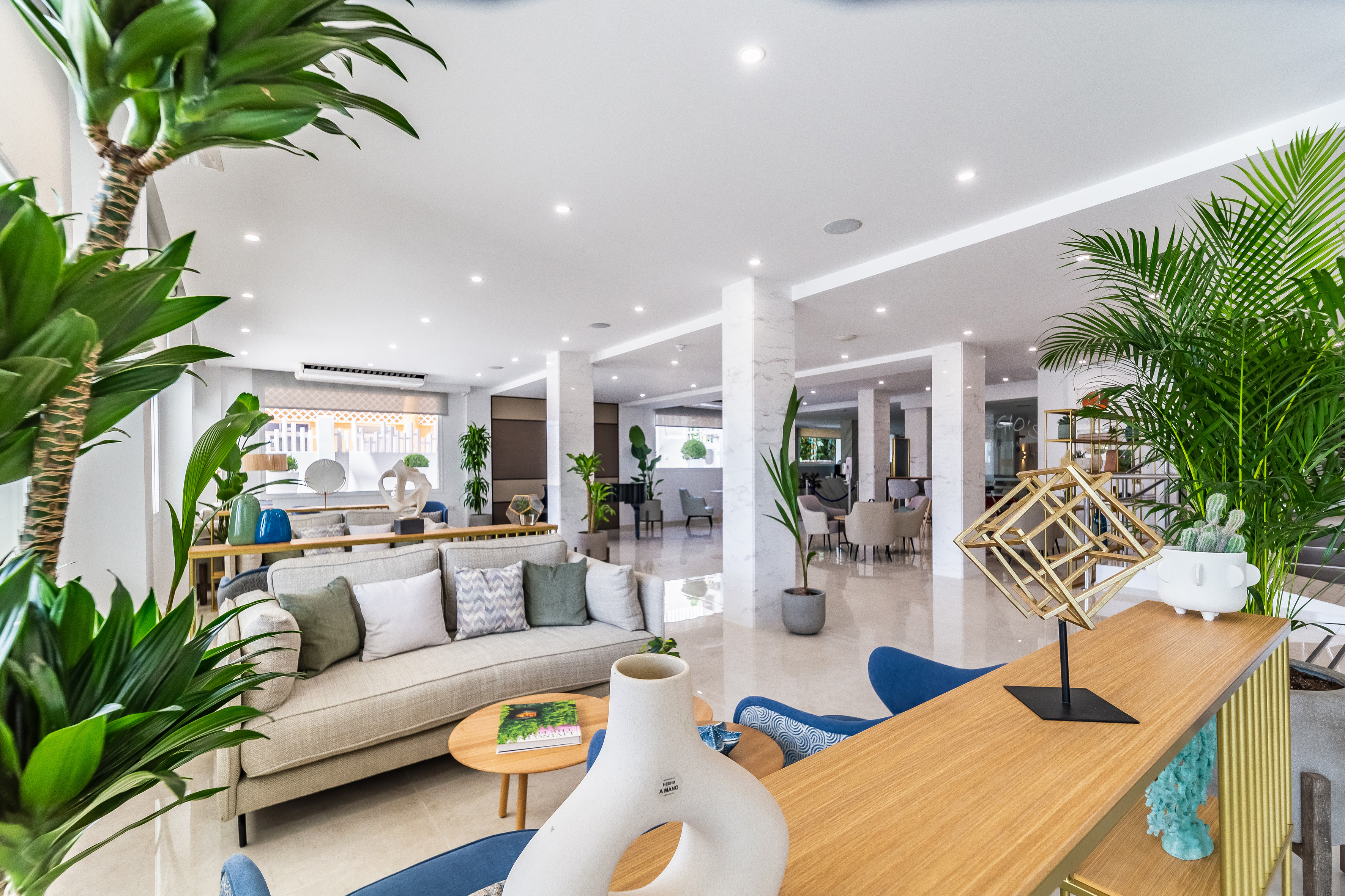 Modern hotel lobby with stylish sofa, lush green plants, and bright decor.