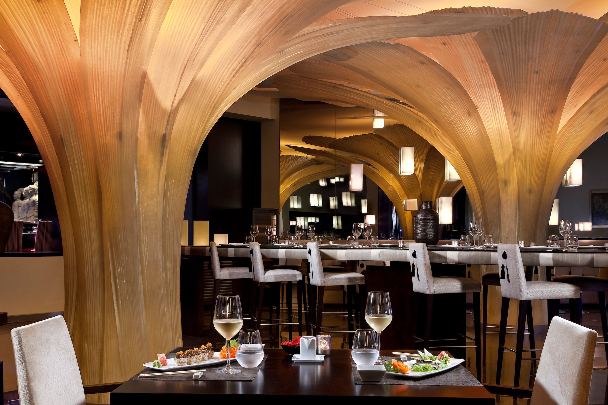 Modern restaurant with unique wooden arches, sushi, and wine on tables.