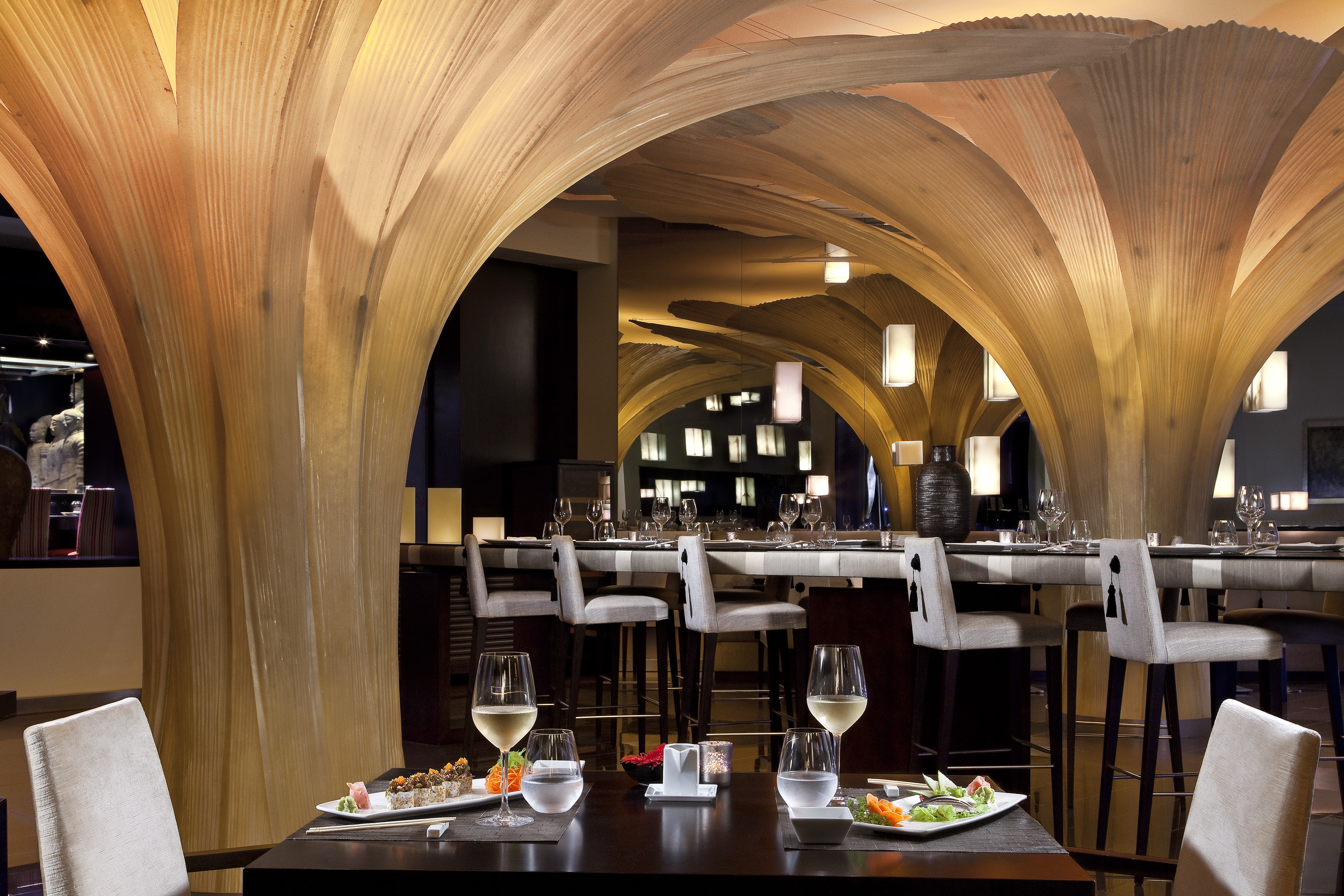 Modern restaurant with unique wooden arches, sushi, and wine on tables.