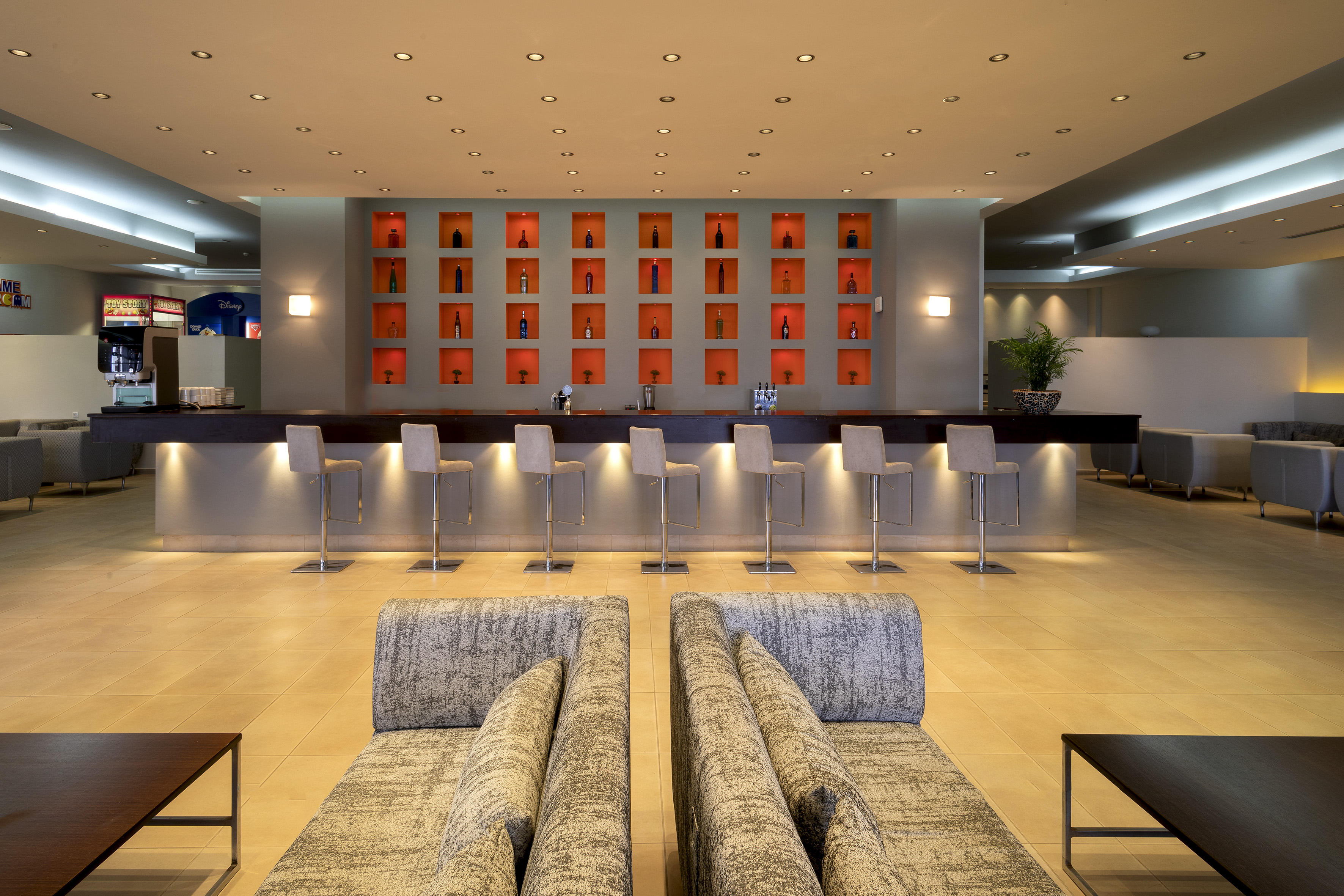 Modern hotel bar with orange bottle display wall, stools, and lounge.