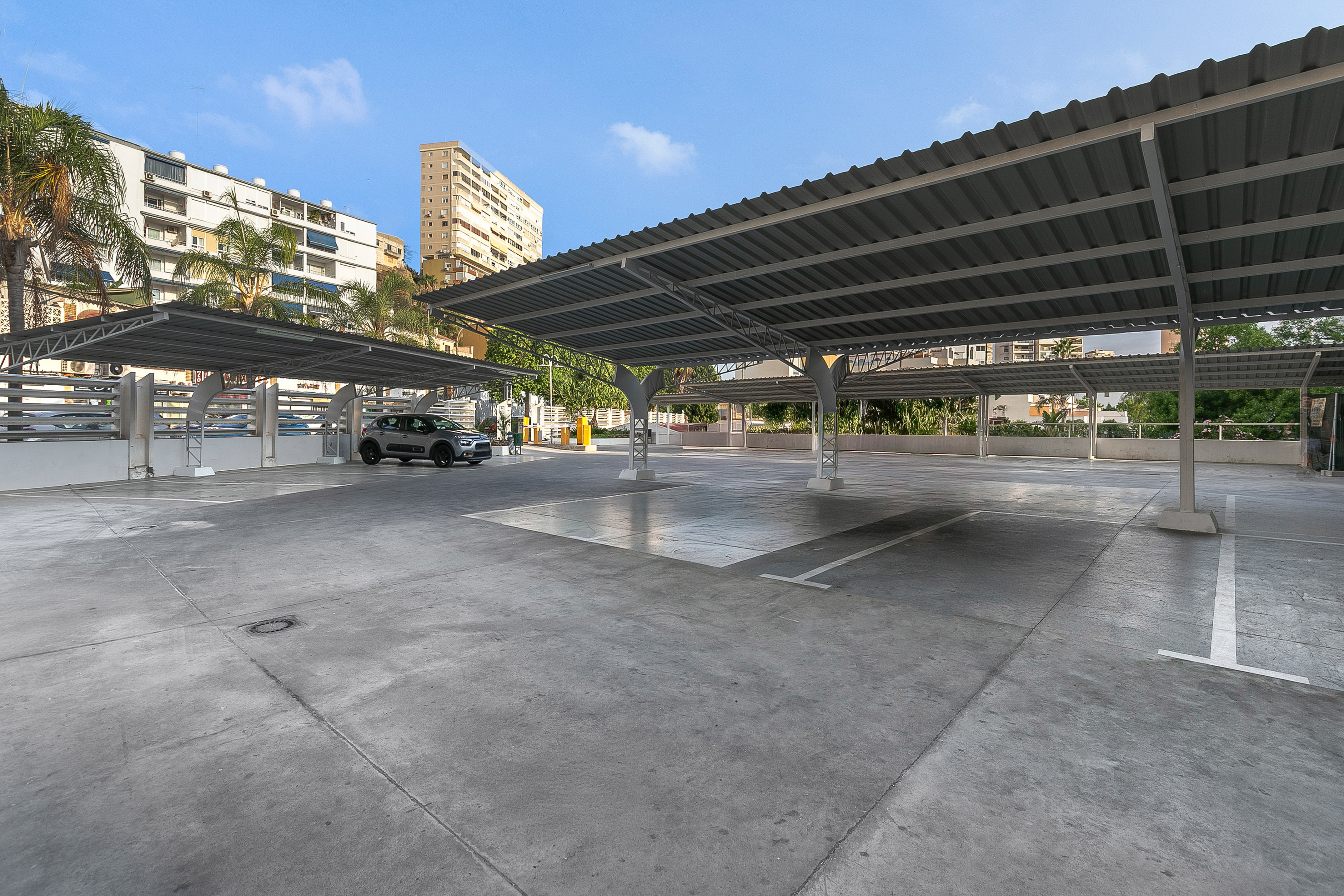 Modern covered outdoor parking lot with one car and apartment buildings.