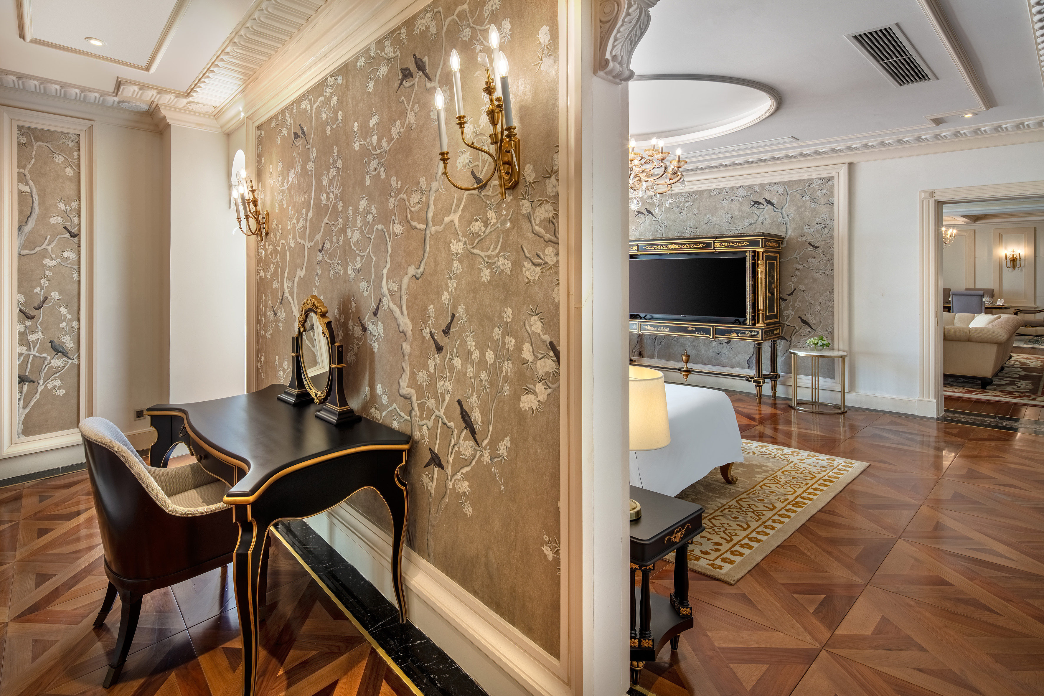Luxury hotel suite with bird wallpaper, vanity, and parquet floor.