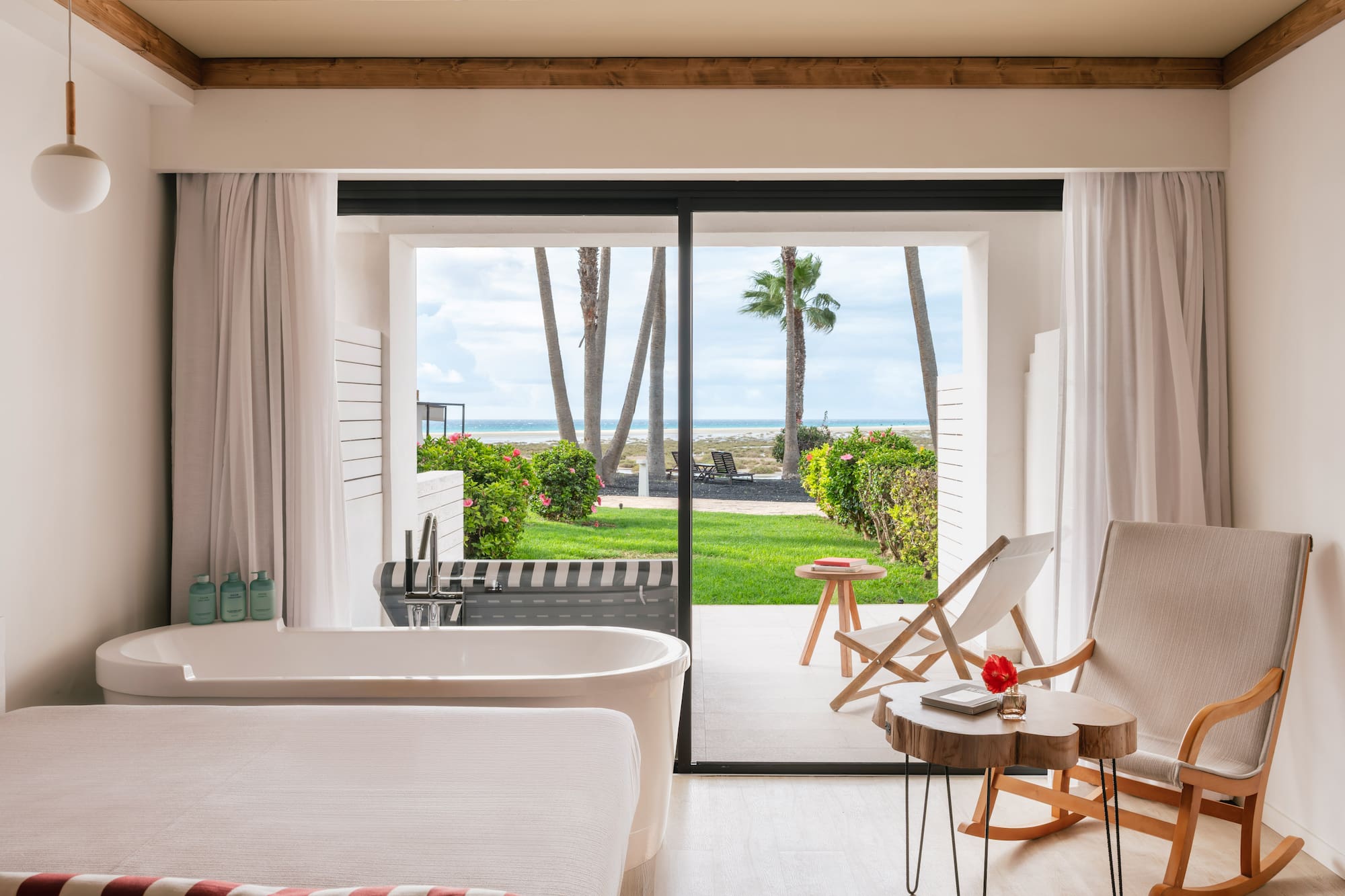Habitación con bañera y vista panorámica al mar, playa y palmeras.