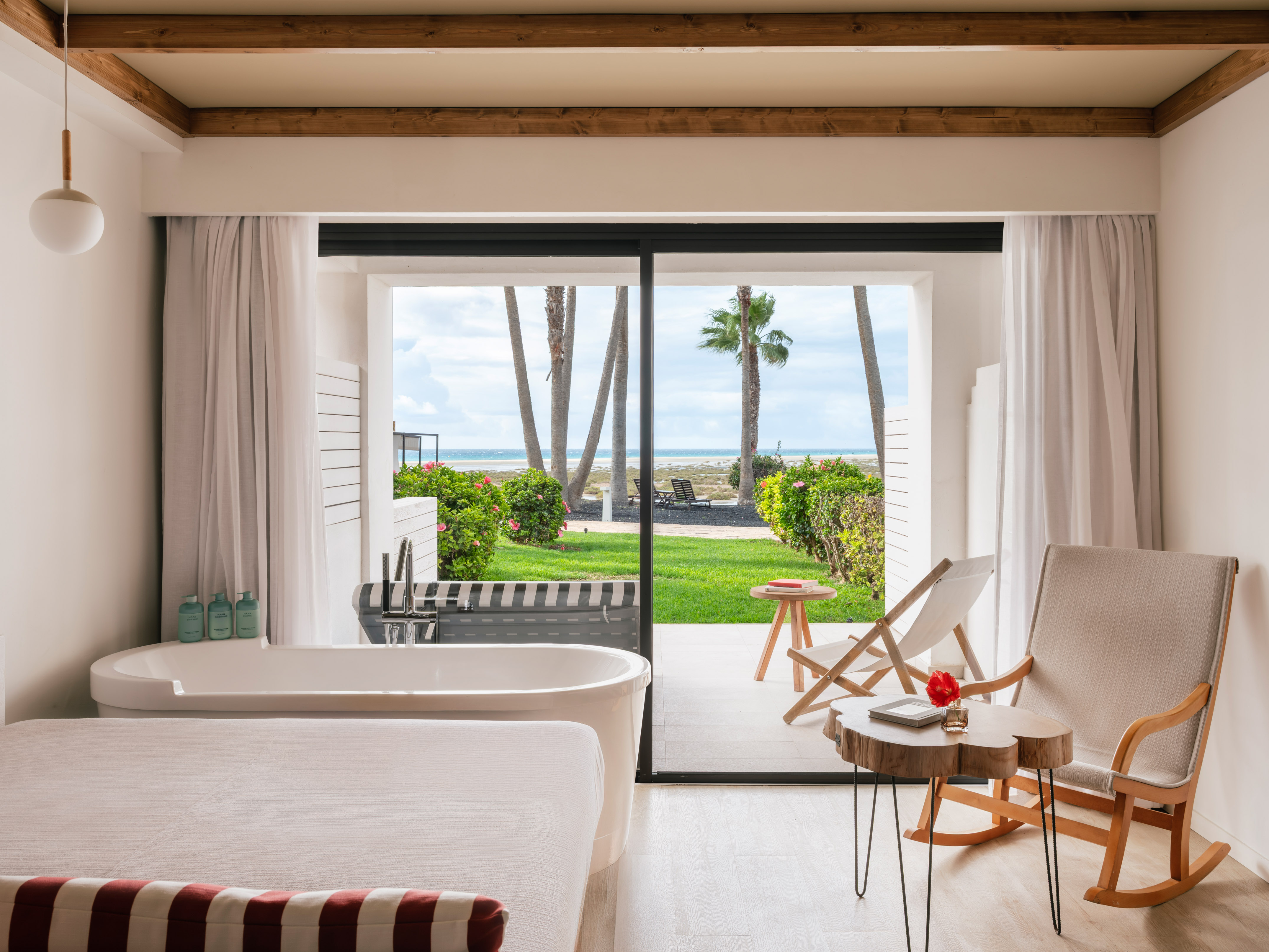 Habitación con bañera y vista panorámica al mar, playa y palmeras.