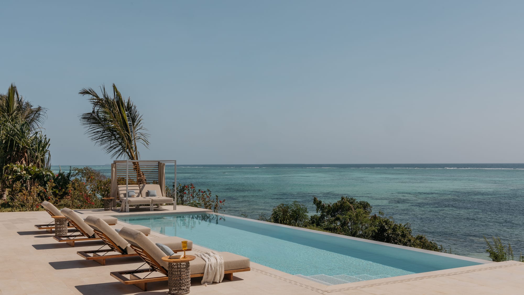 a pool with lounge chairs and a palm tree overlooking the ocean