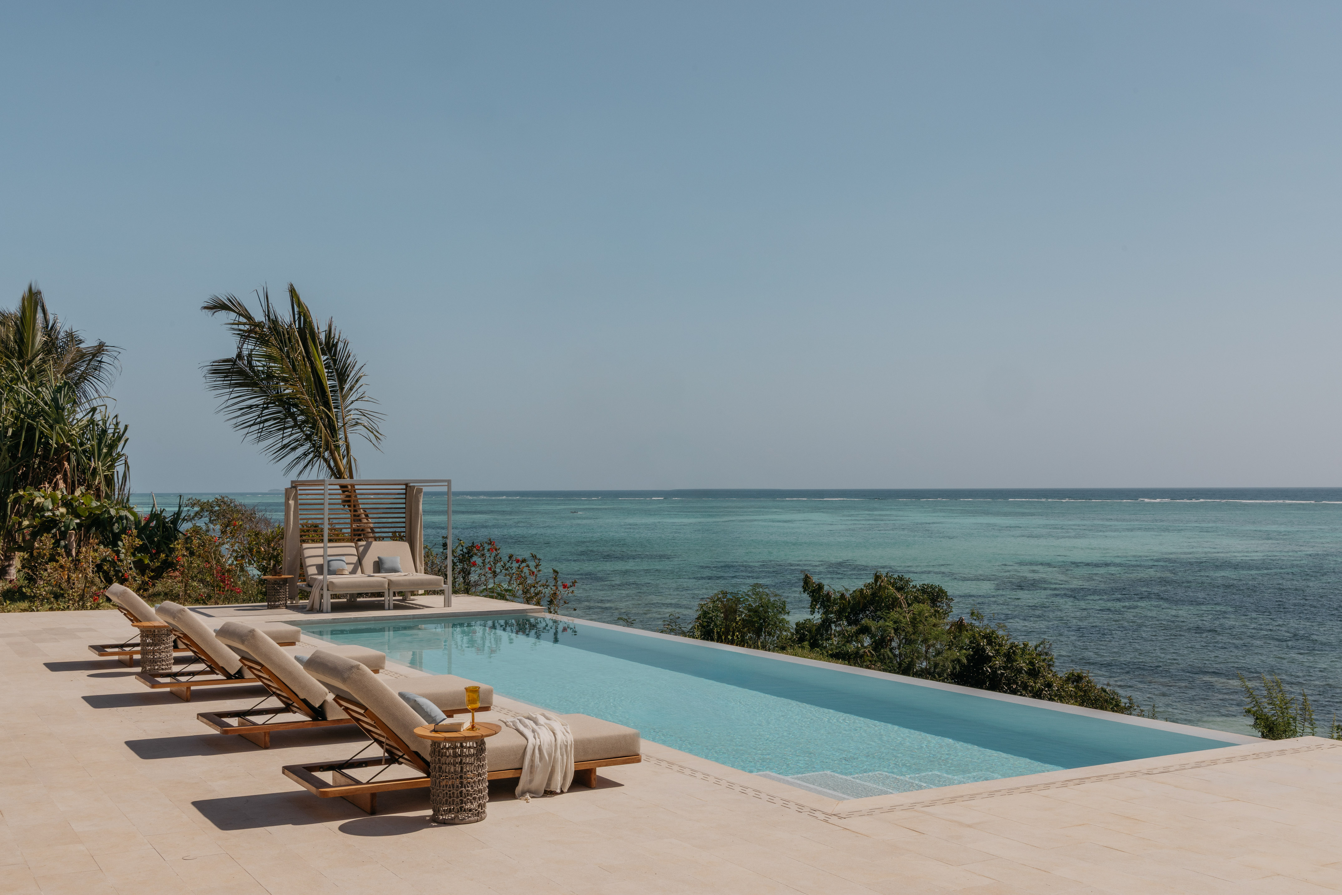a pool with lounge chairs and a palm tree overlooking the ocean