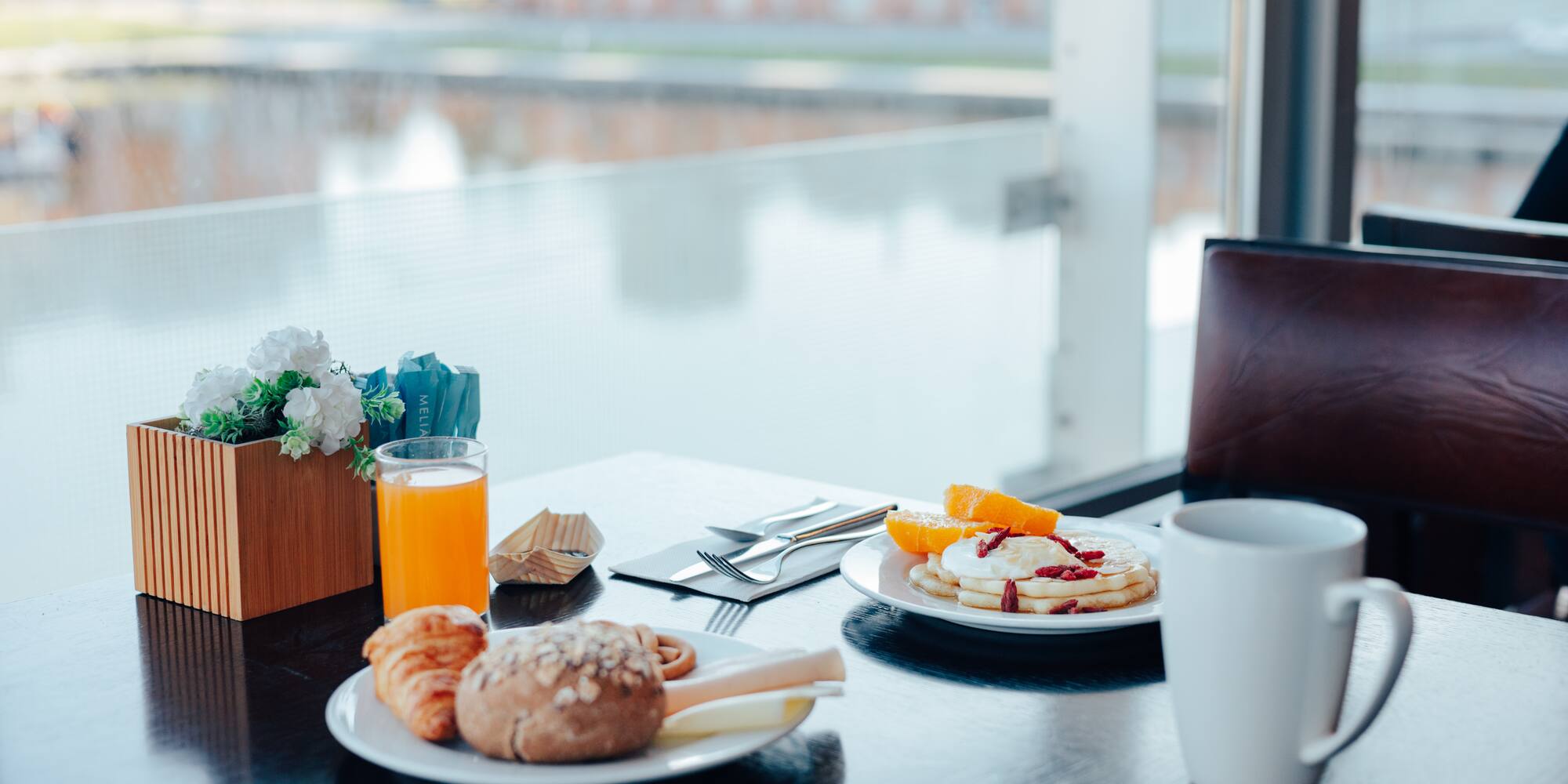 Meliá hotel breakfast: pancakes, croissant, orange juice, scenic view.
