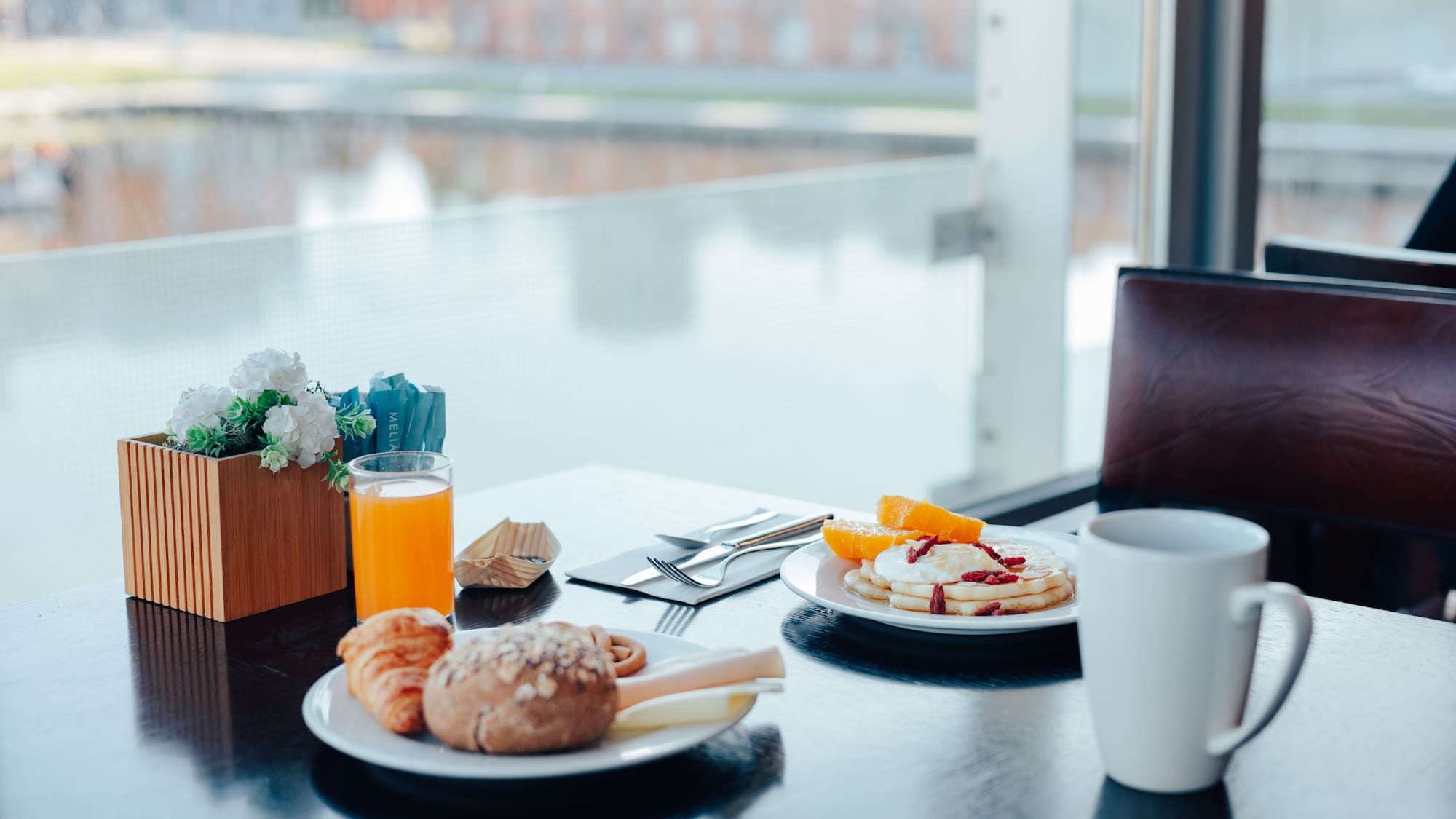 Meliá hotel breakfast: pancakes, croissant, orange juice, scenic view.