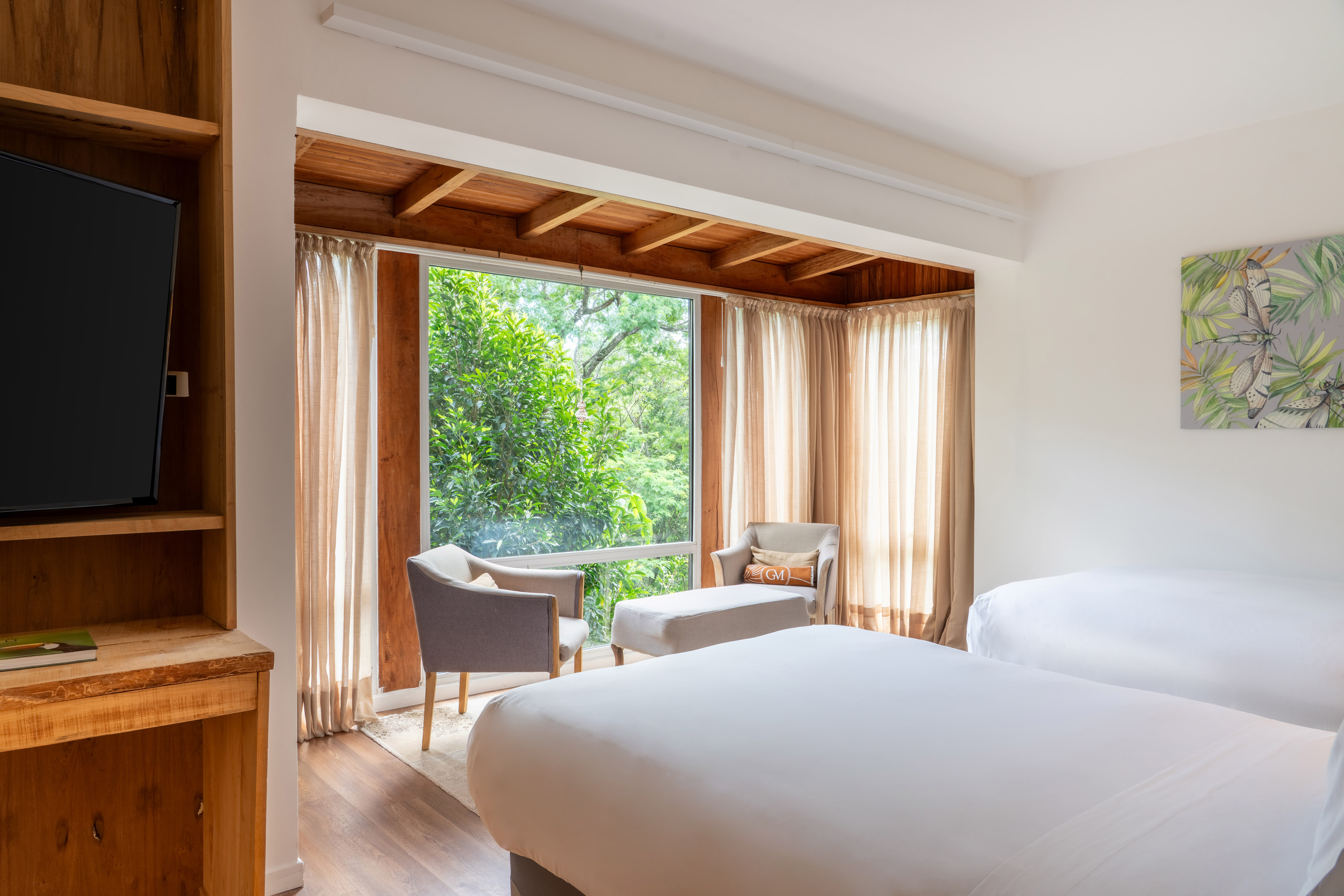 Cozy bedroom with two beds, large window, green trees, and warm wooden accents.