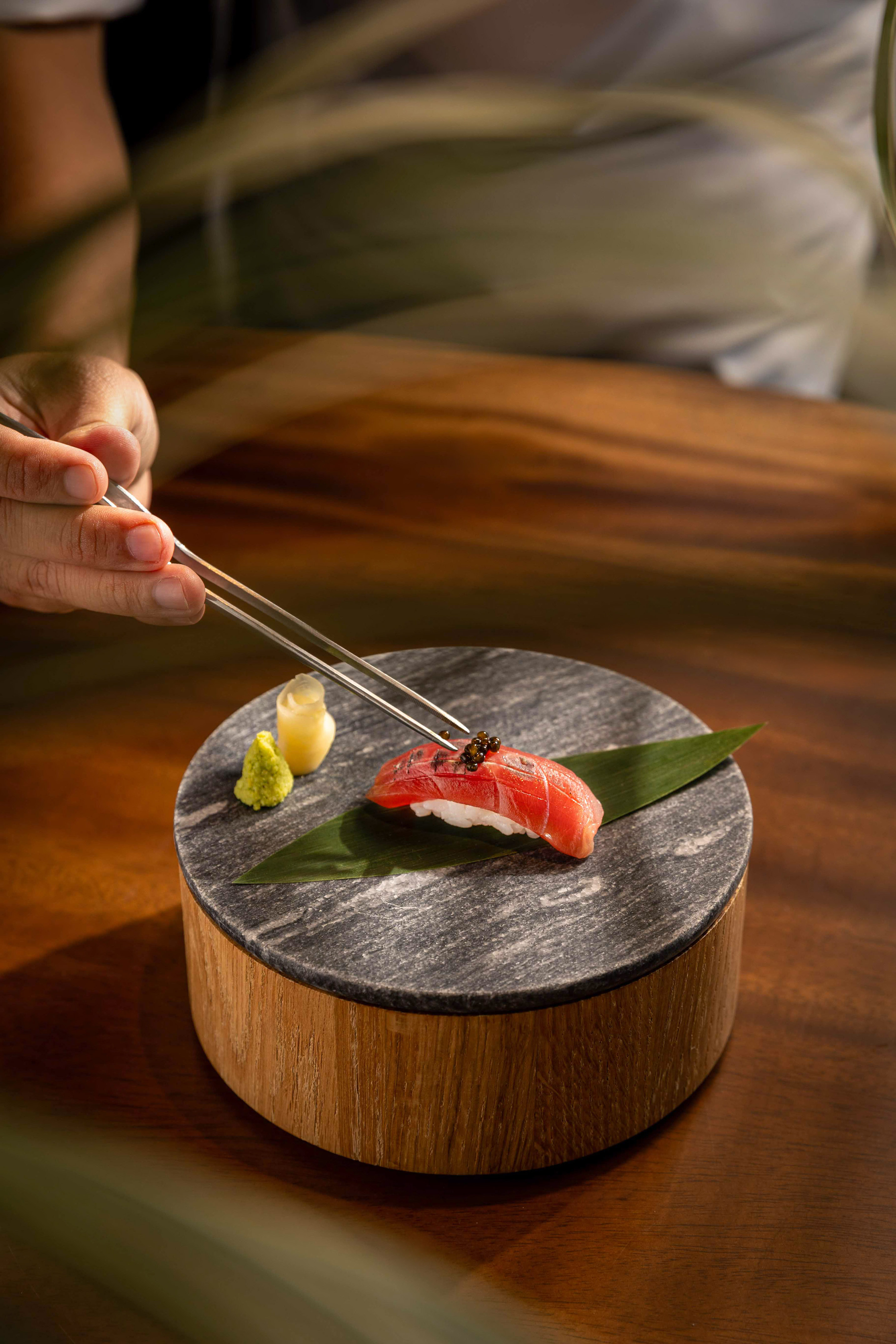 Chef garnishing tuna nigiri sushi with caviar, wasabi, and ginger on a stone plate.