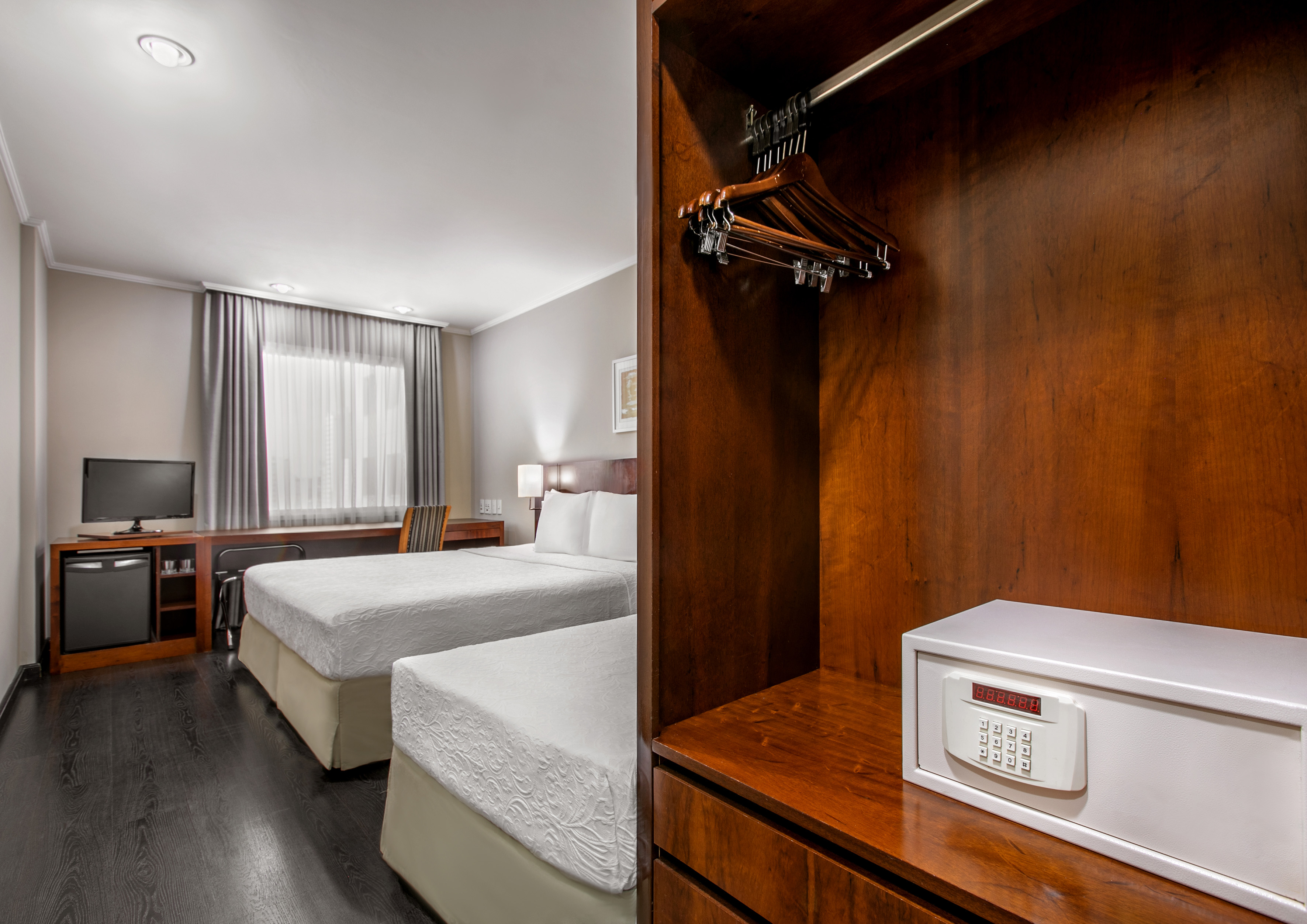Hotel room with two beds, desk, TV, mini-fridge, and wardrobe safe.