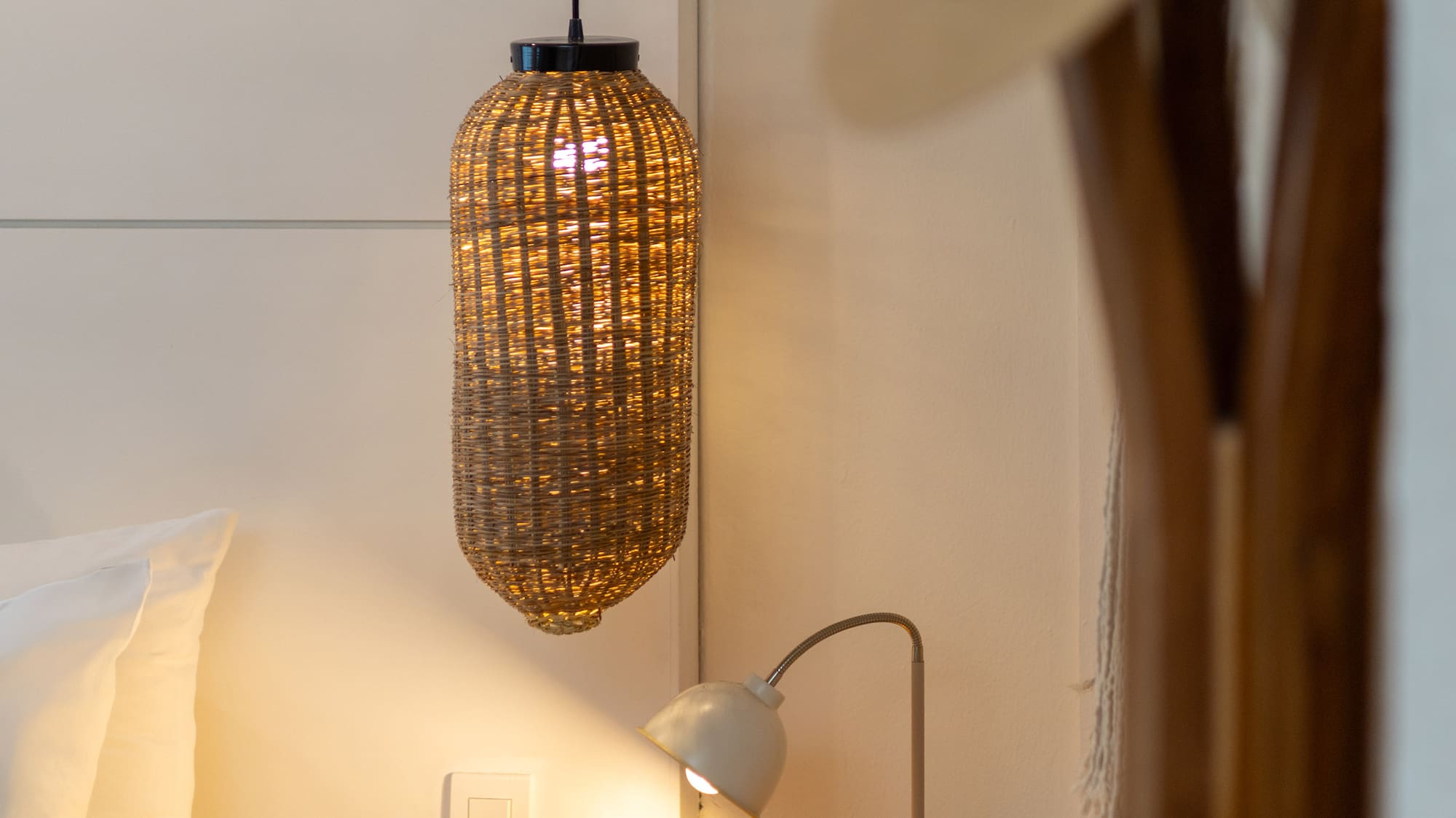 Dormitorio con mesita de noche de madera, lámpara de ratán y luz cálida.