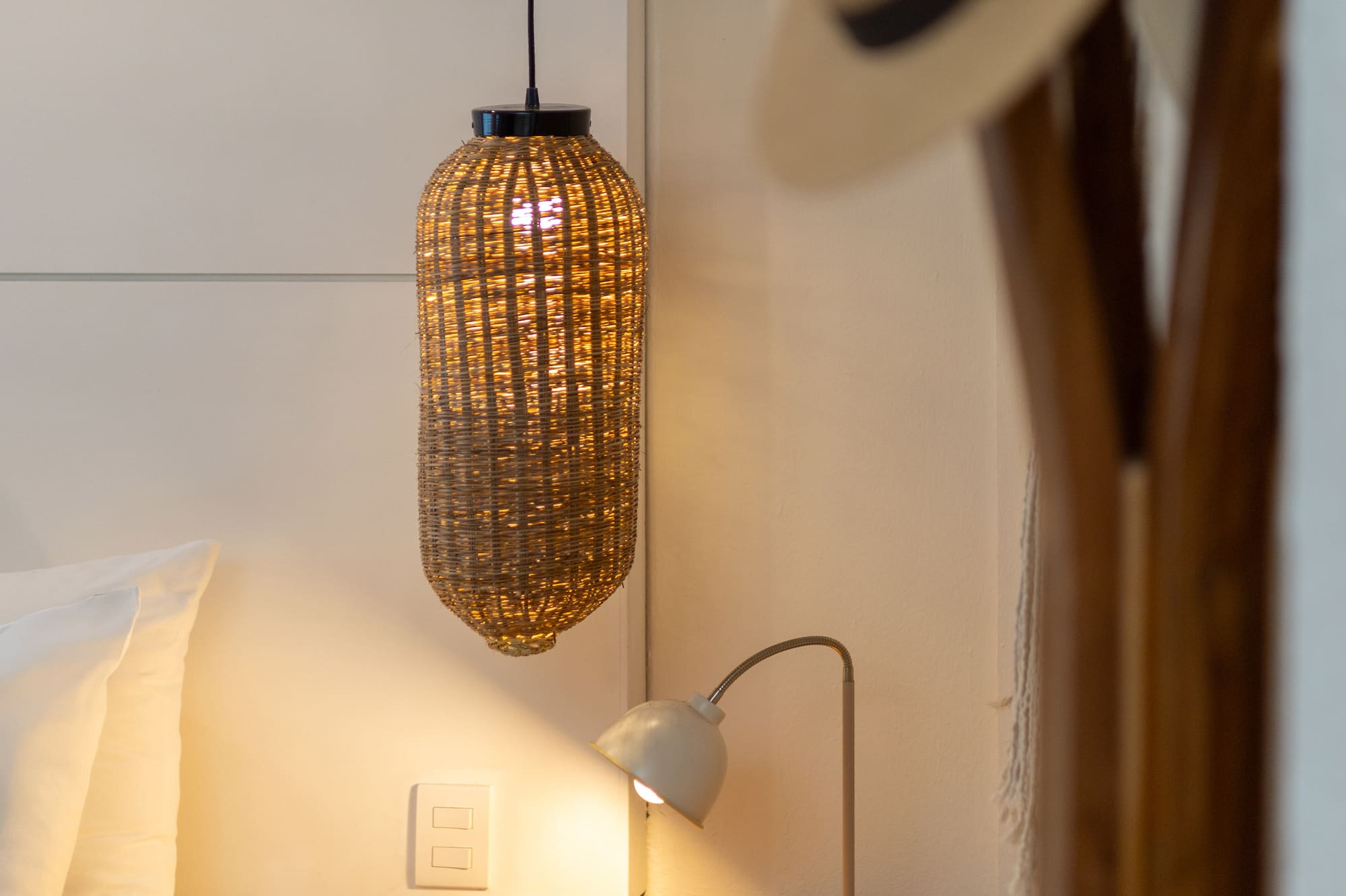 Dormitorio con mesita de noche de madera, lámpara de ratán y luz cálida.
