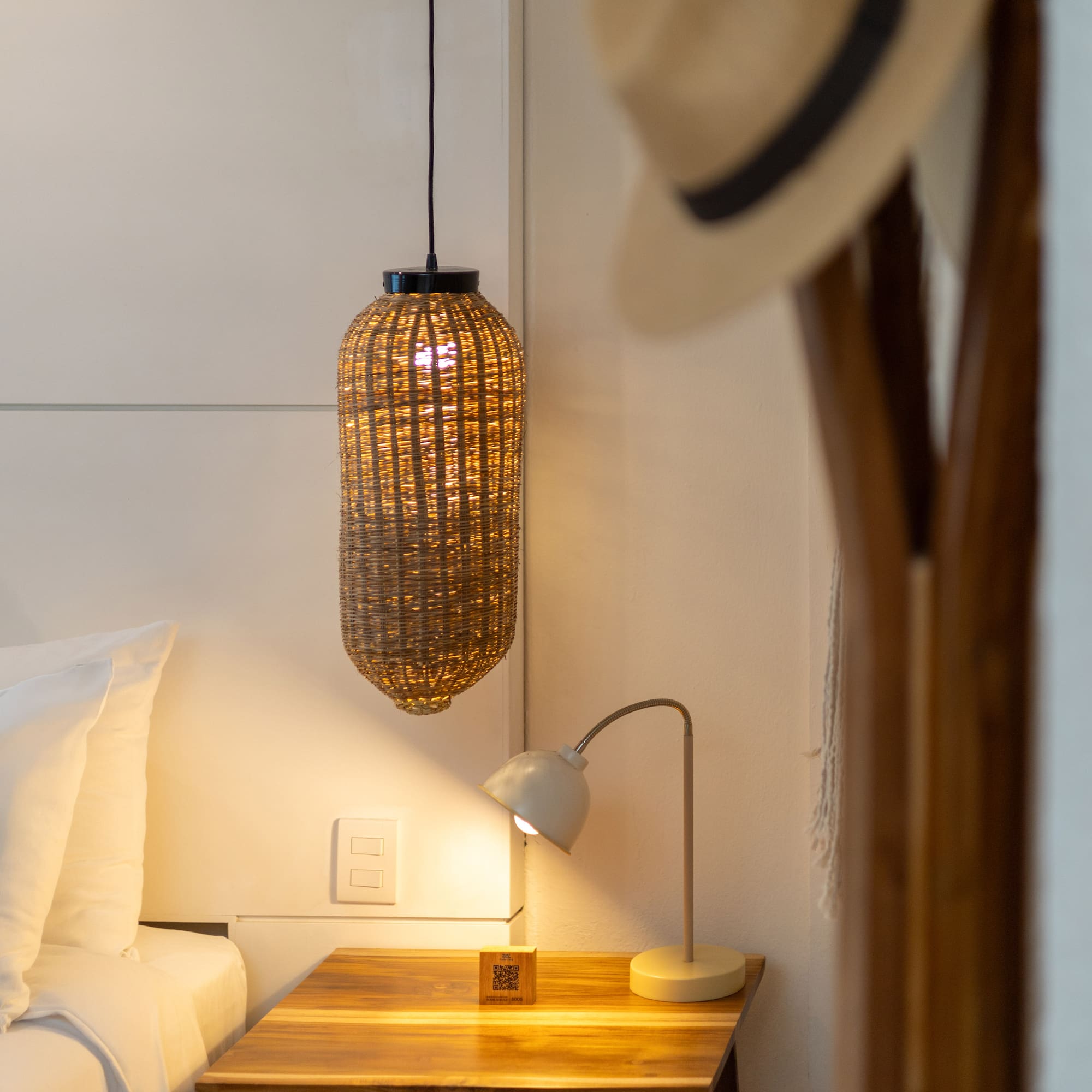 Dormitorio con mesita de noche de madera, lámpara de ratán y luz cálida.