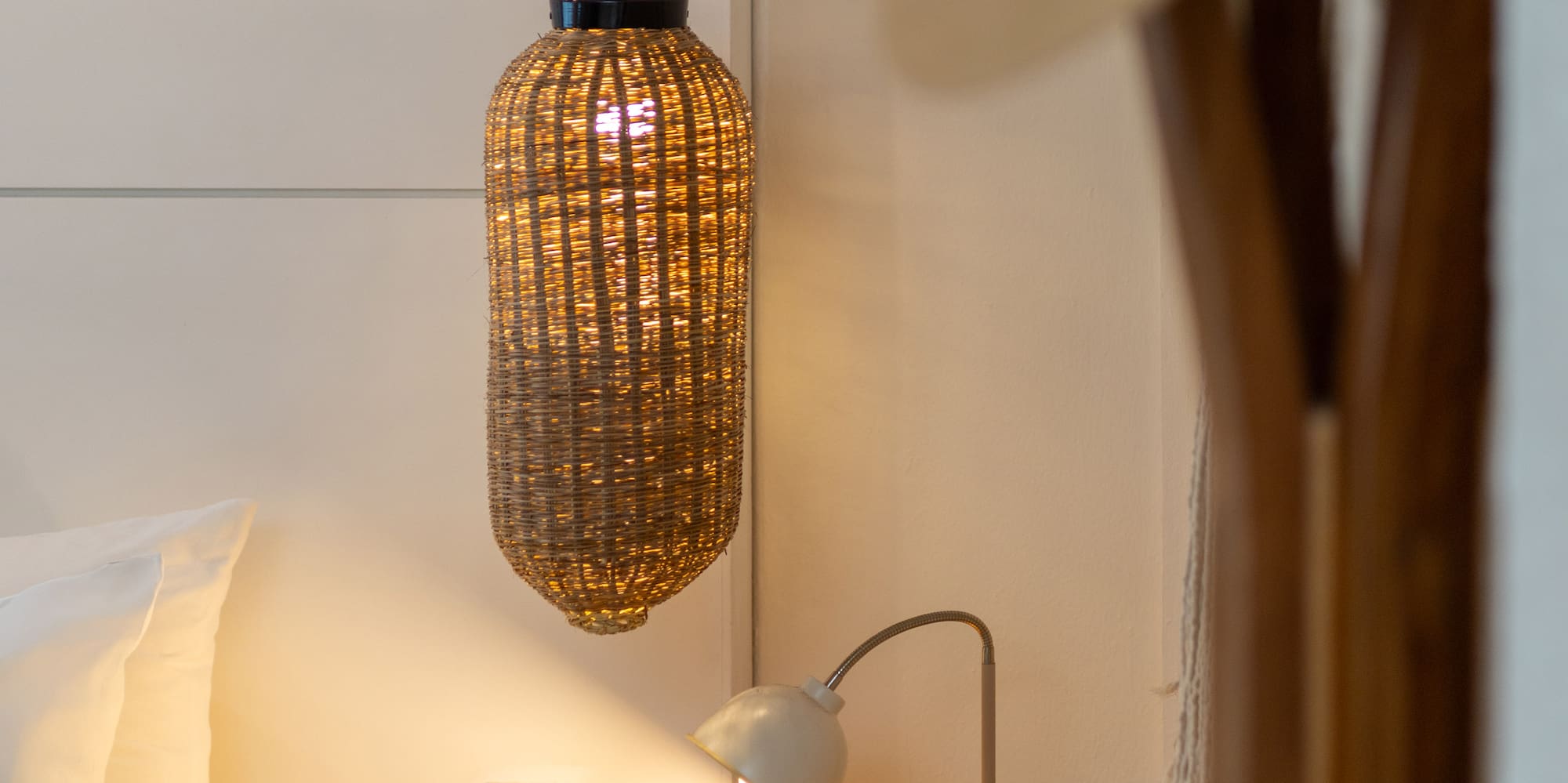 Dormitorio con mesita de noche de madera, lámpara de ratán y luz cálida.