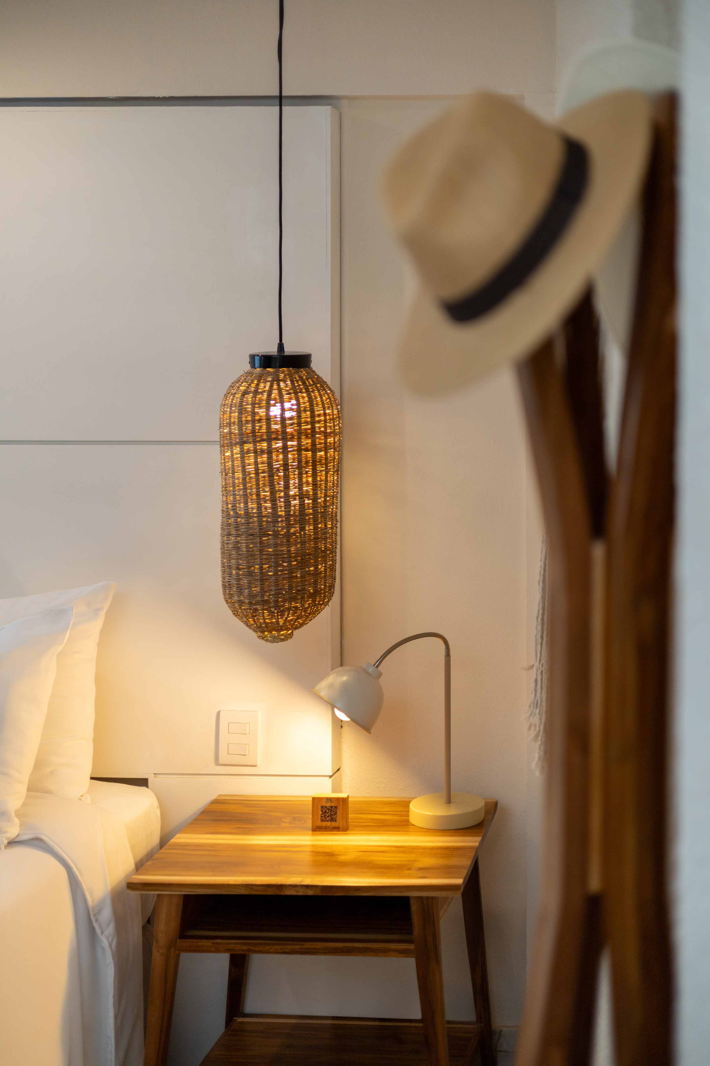 Dormitorio con mesita de noche de madera, lámpara de ratán y luz cálida.