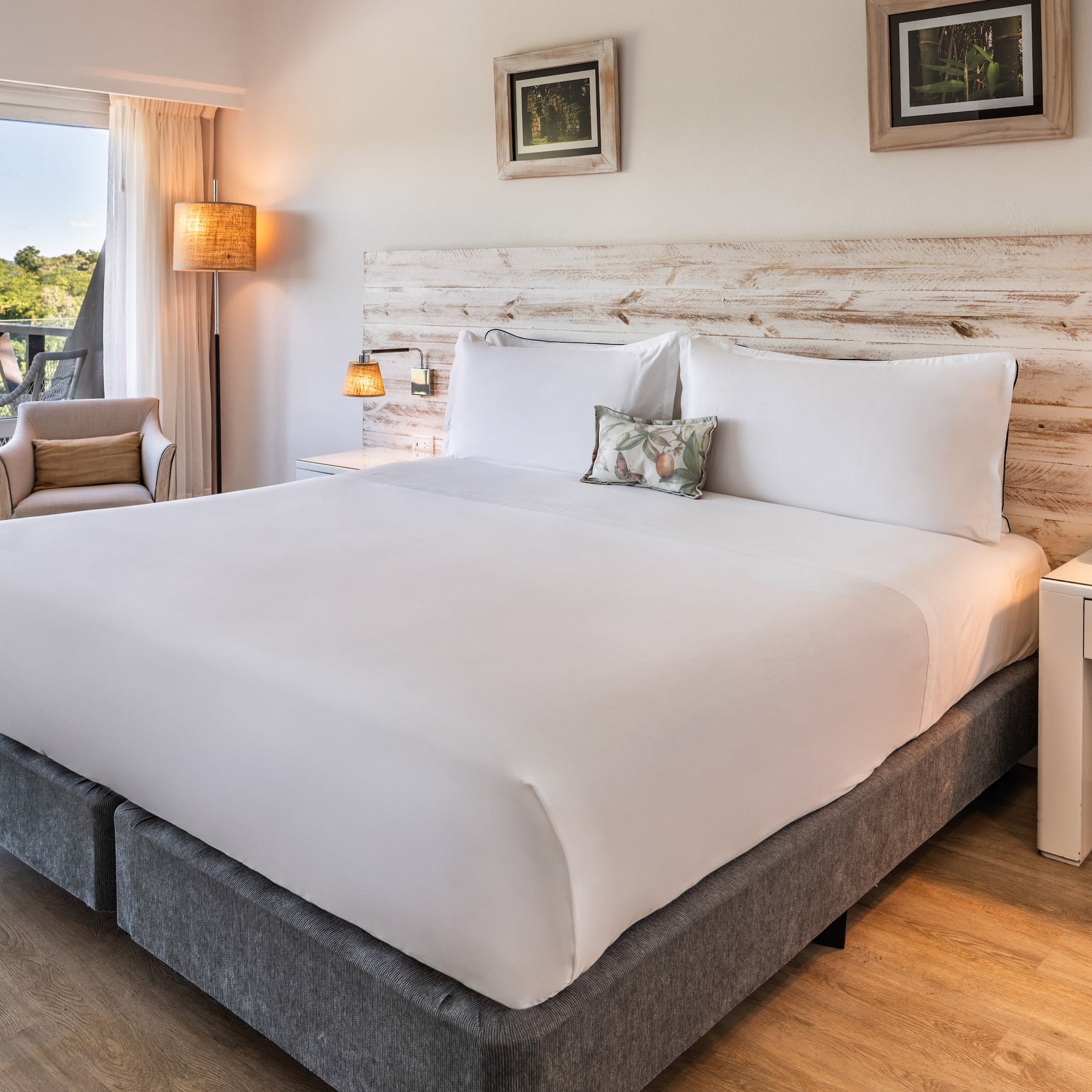 a bed with white sheets and pillows in a room with a deck and chairs