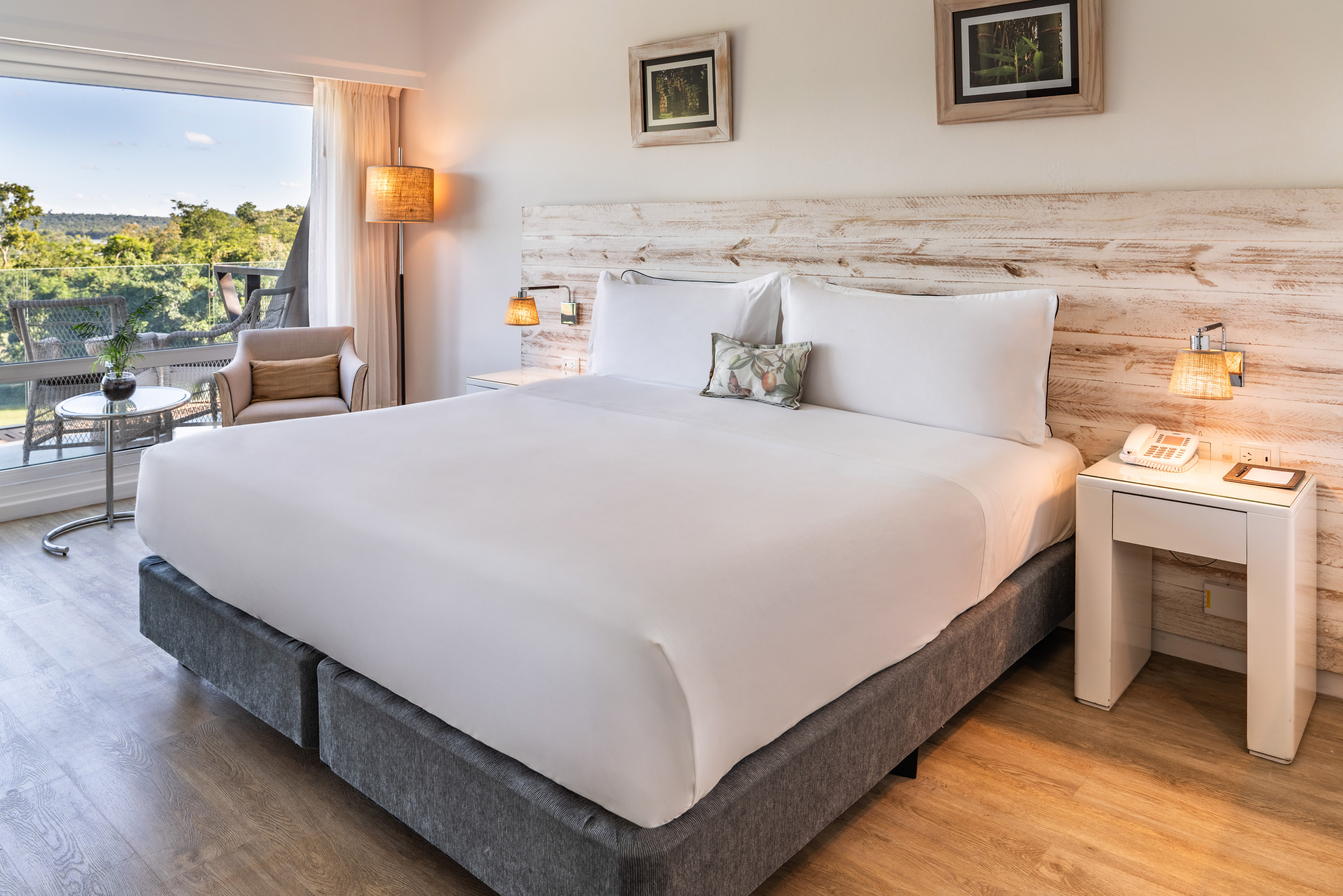 a bed with white sheets and pillows in a room with a deck and chairs