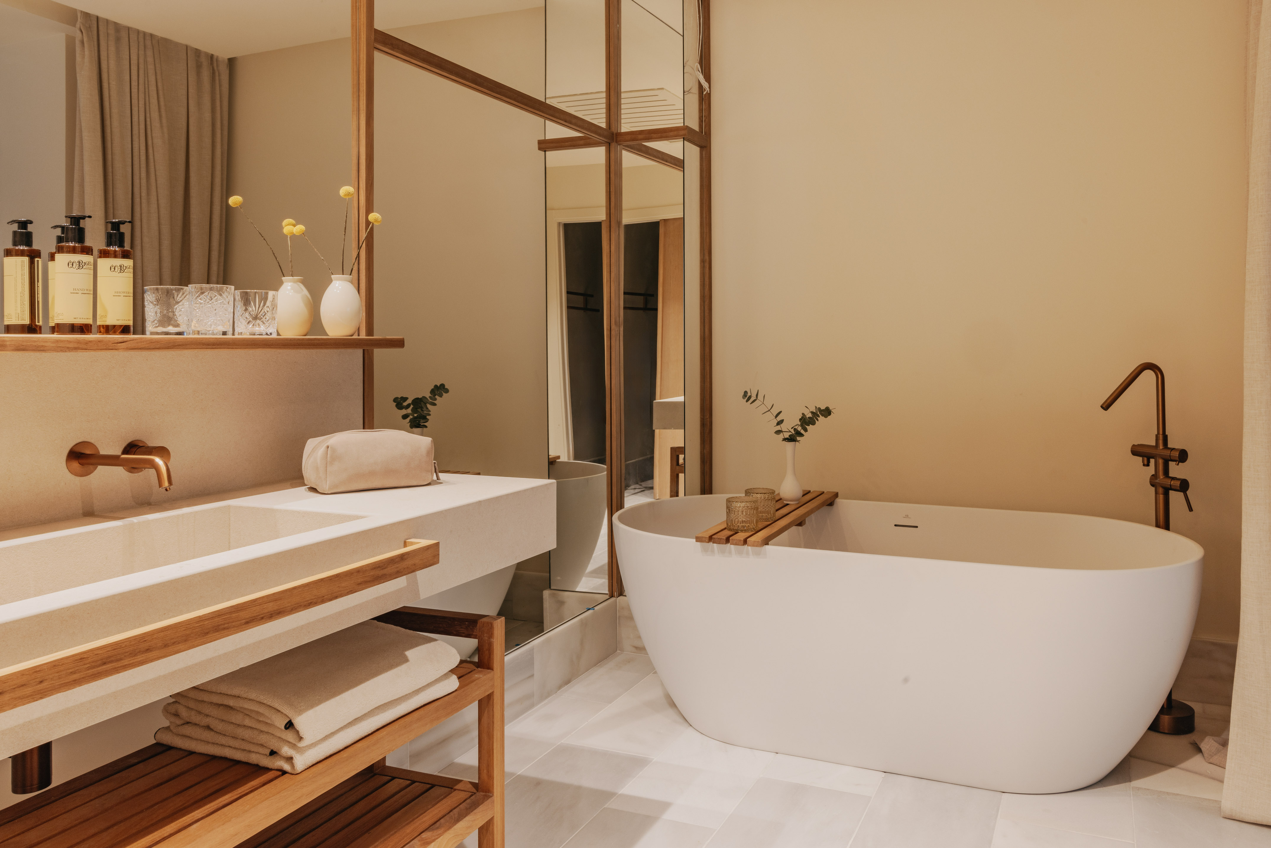 Modern bathroom with freestanding tub, stone vanity, copper fixtures, wood details.