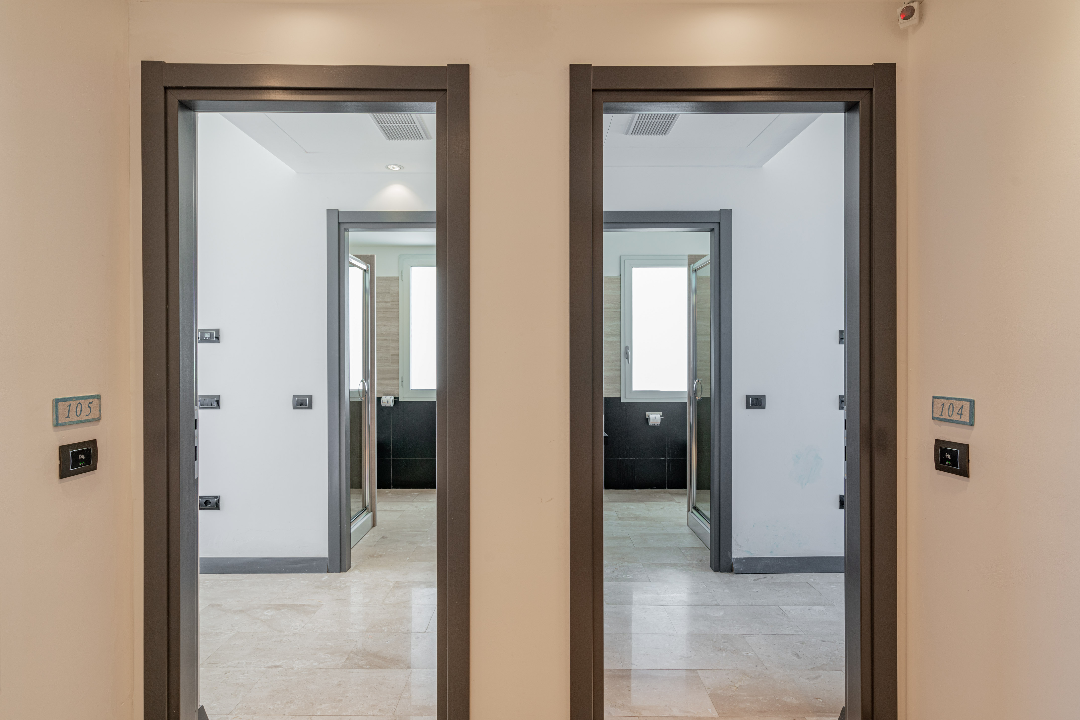Open doors to modern hotel rooms 104, 105; bright interiors, tiled floors.