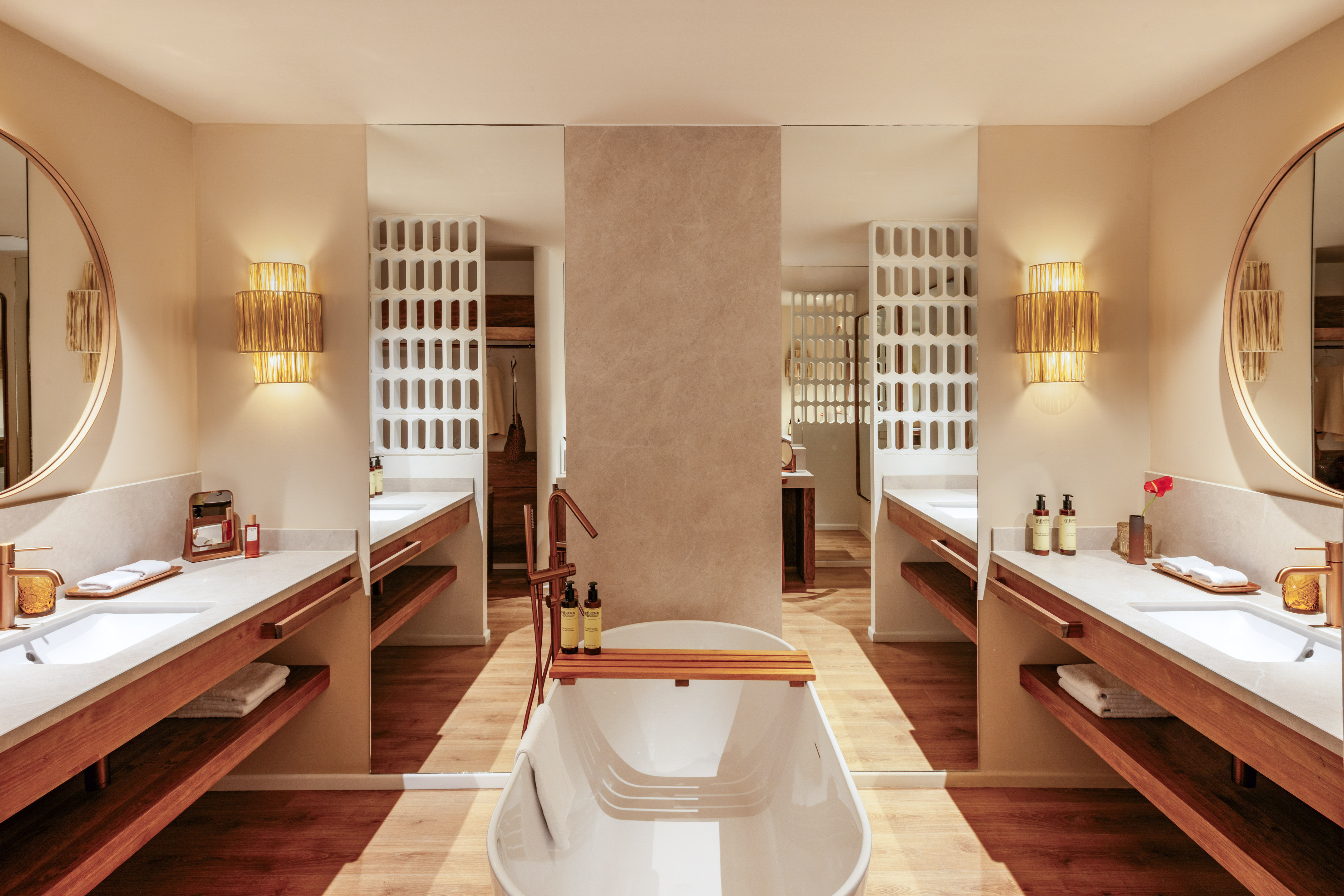 Modern luxury bathroom with freestanding tub, dual vanities, and warm wood accents.