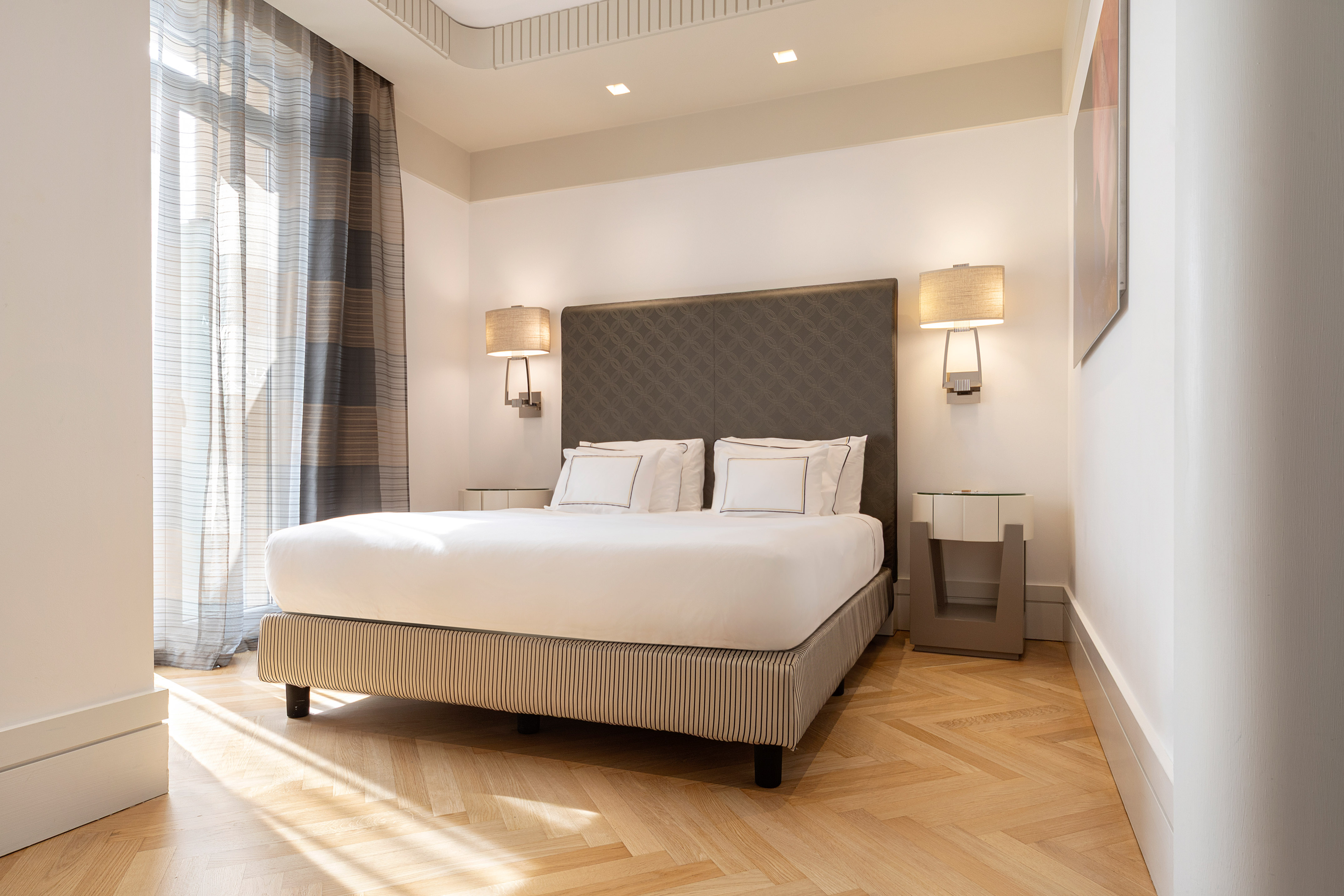 Modern hotel bedroom with king bed, white linens, and herringbone wood floor.