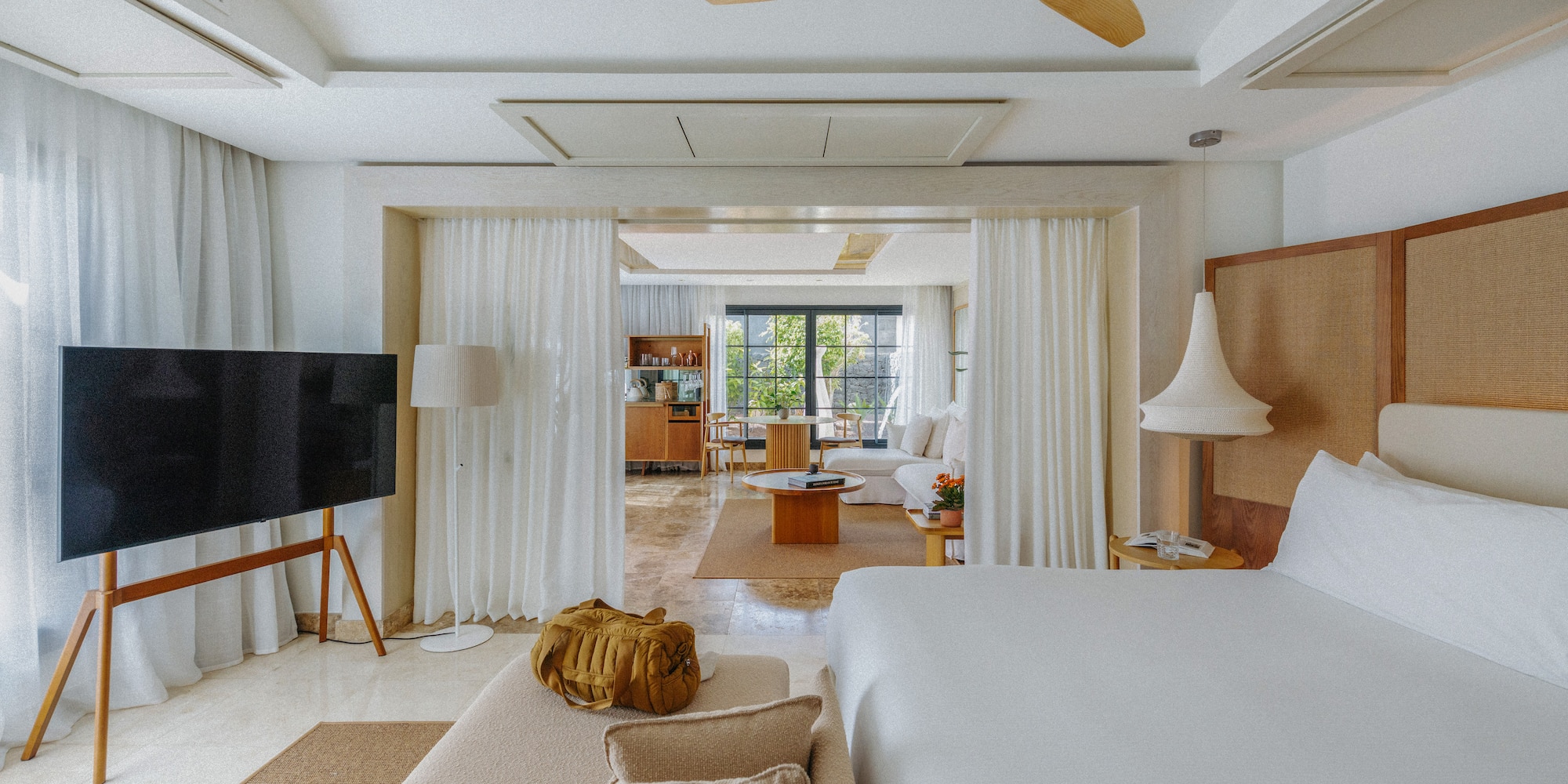 Bright, open-plan modern hotel suite with bedroom, living area, and TV.