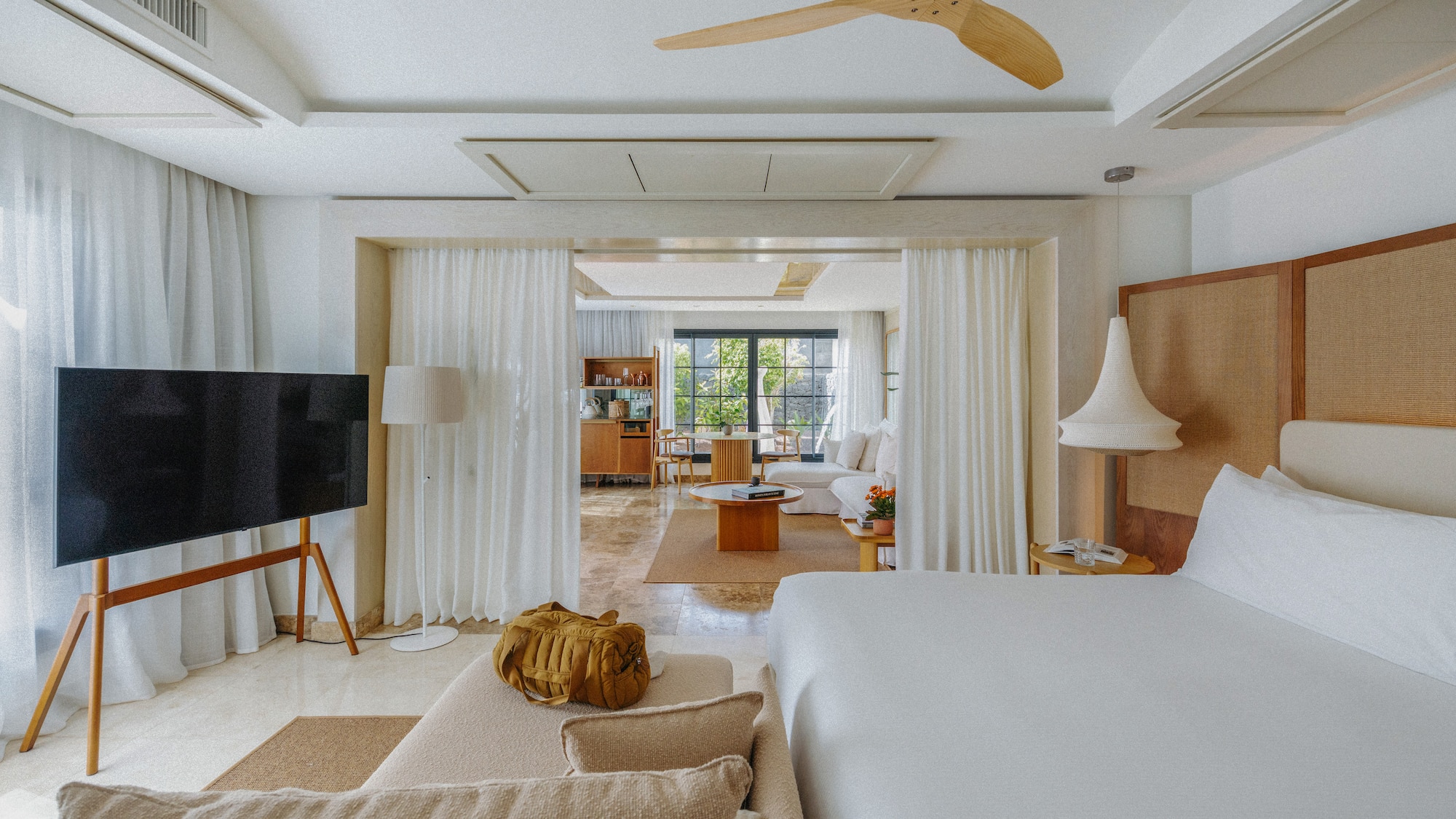 Bright, open-plan modern hotel suite with bedroom, living area, and TV.