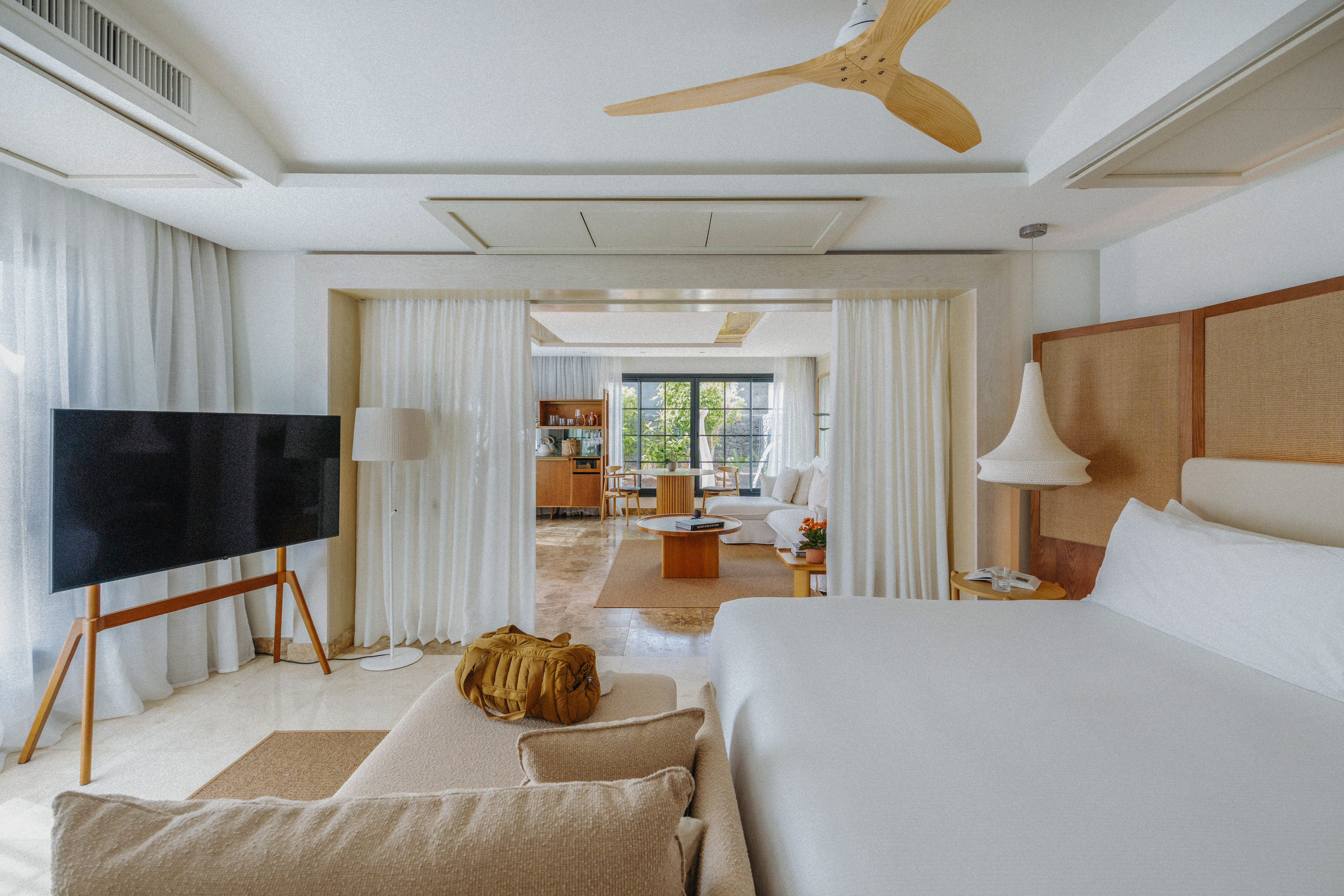 Bright, open-plan modern hotel suite with bedroom, living area, and TV.