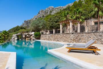 Luxury swimming pool, mountain backdrop, palm trees, and sun loungers.