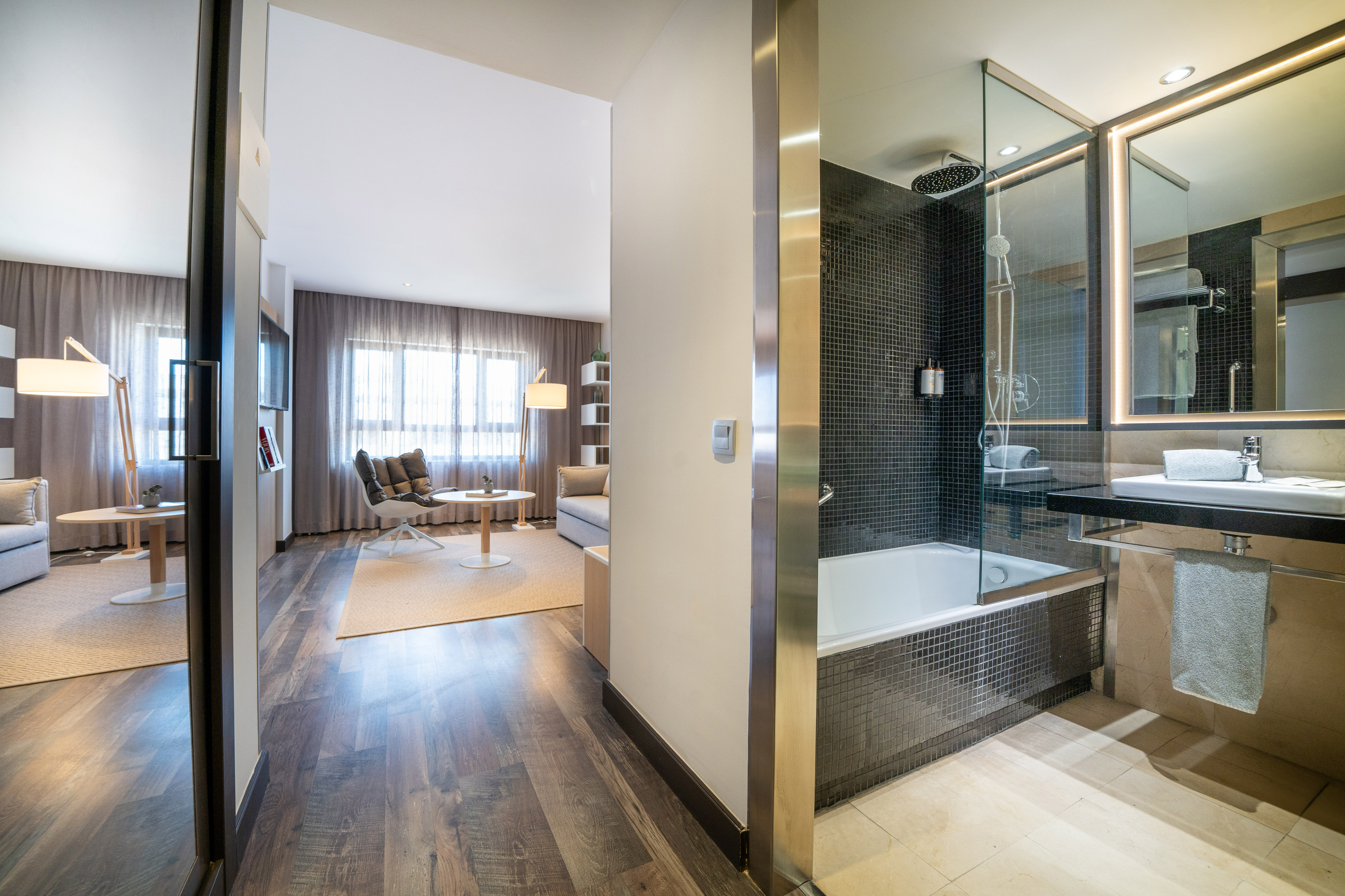Modern hotel suite with living area and bathroom, featuring bathtub and shower.