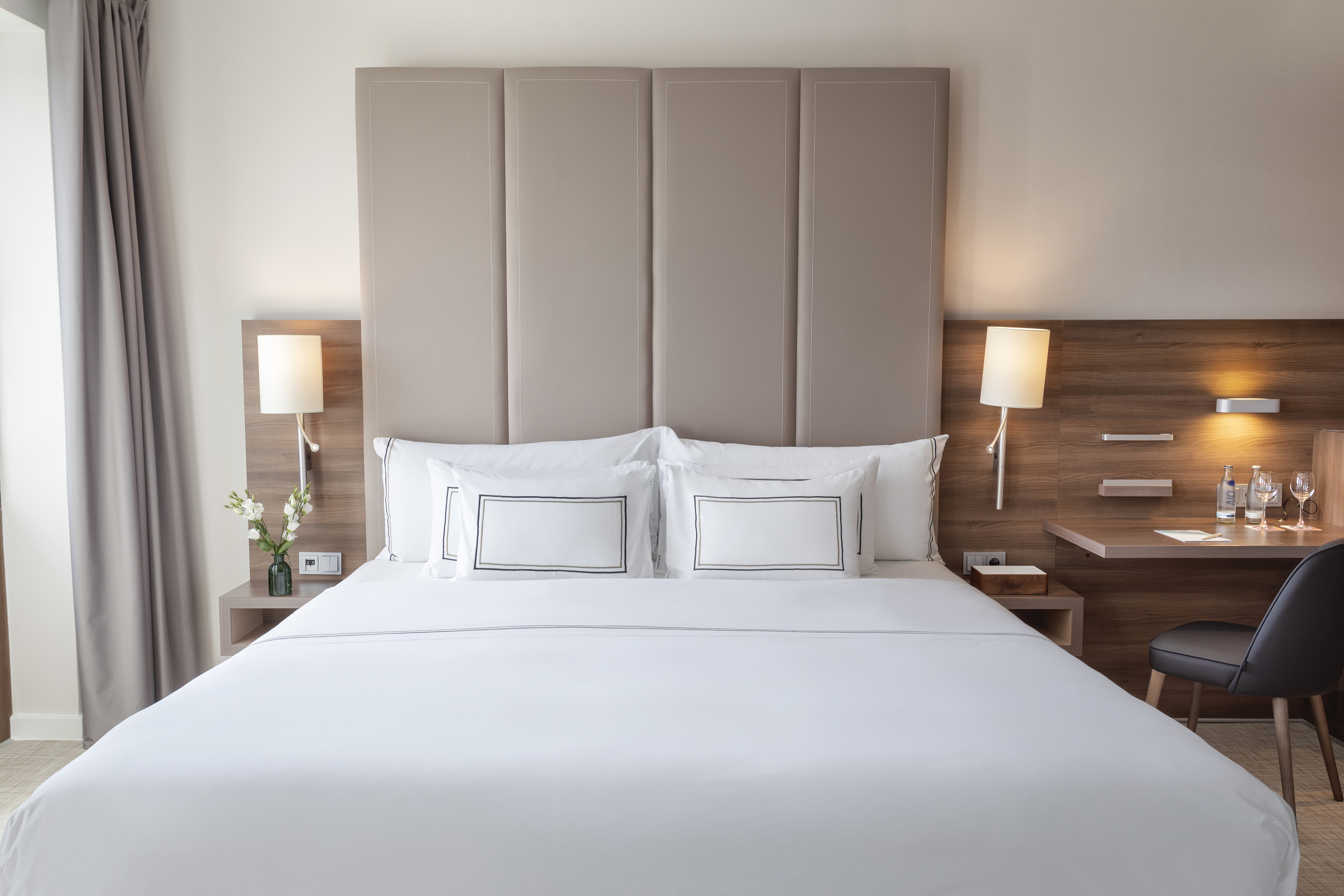 Clean modern hotel room with king bed, beige upholstered headboard, and desk.
