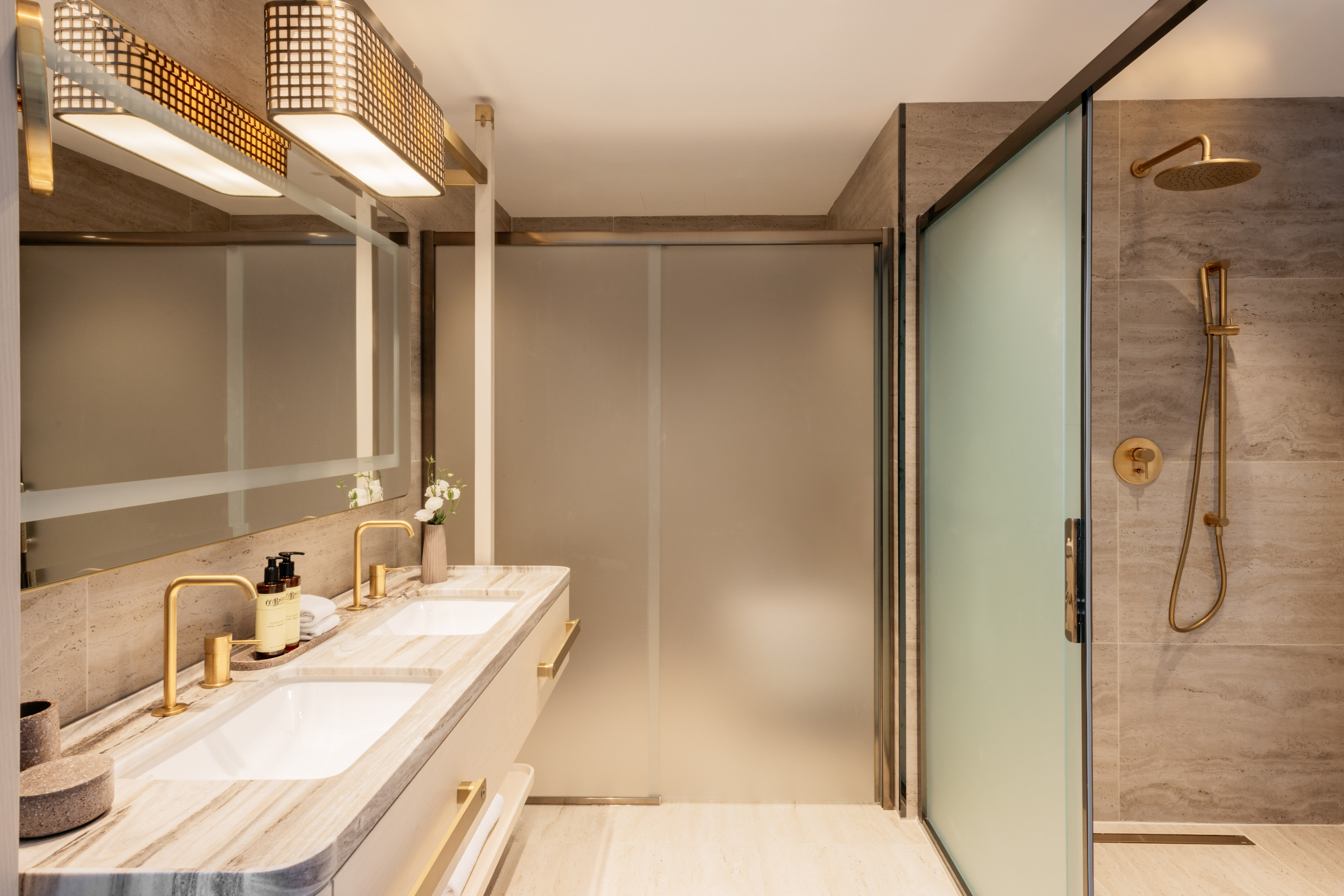 Modern bathroom with marble double vanity, gold fixtures, glass shower.