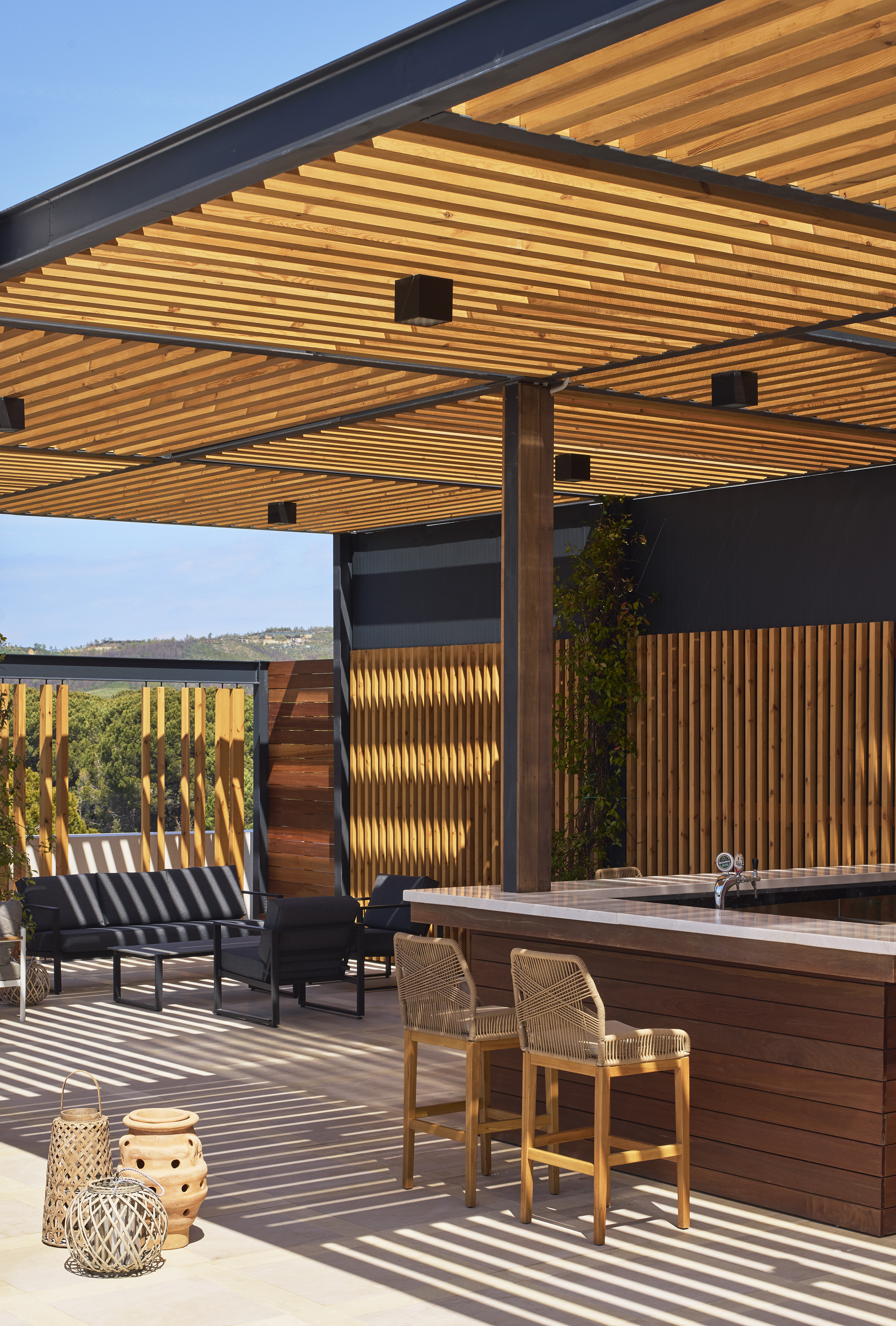 Modern outdoor patio bar, wooden slat pergola, lounge seating, sunlit ambiance.