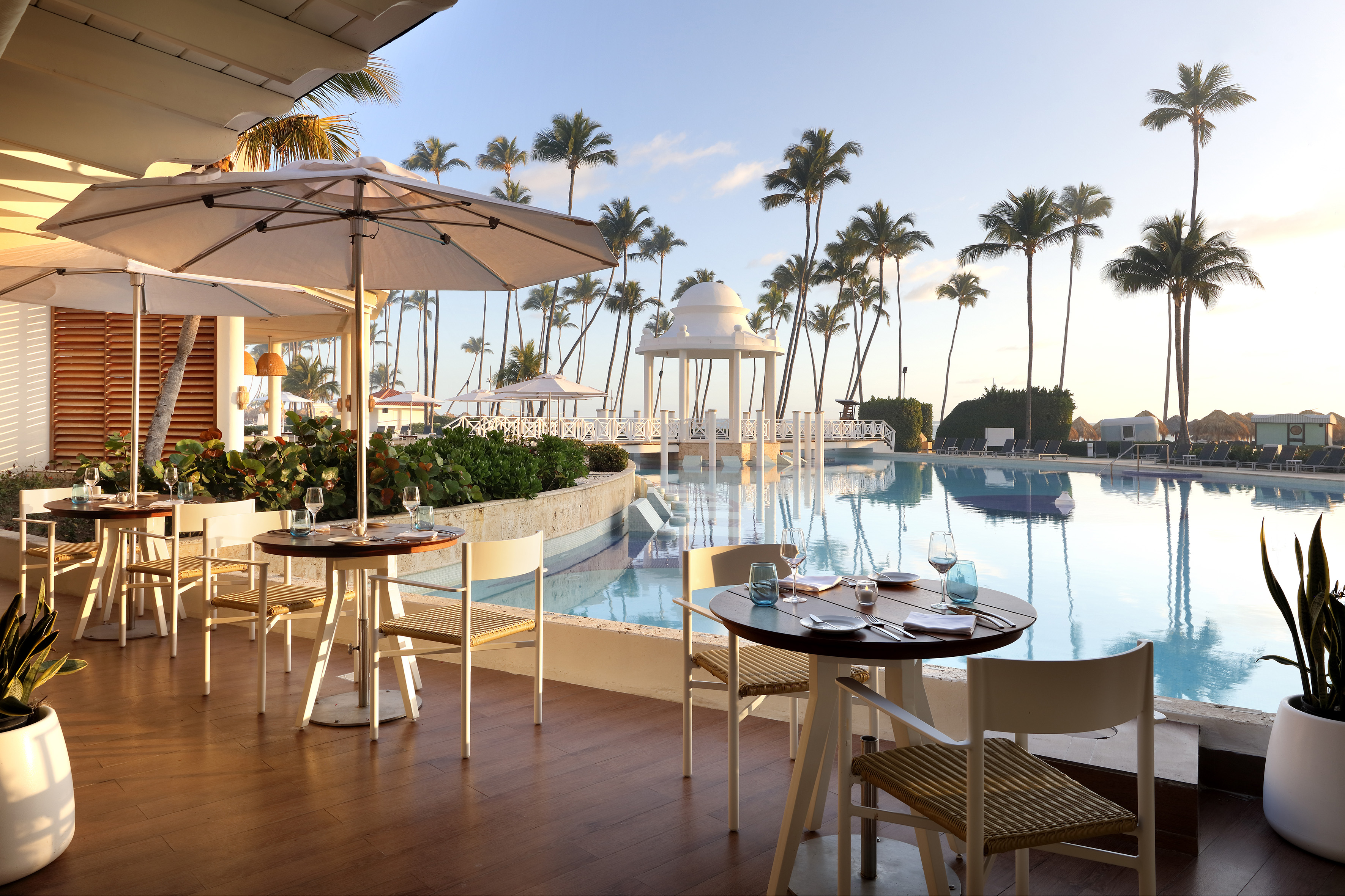 Poolside restaurant tables and umbrellas at a tropical resort with palm trees.