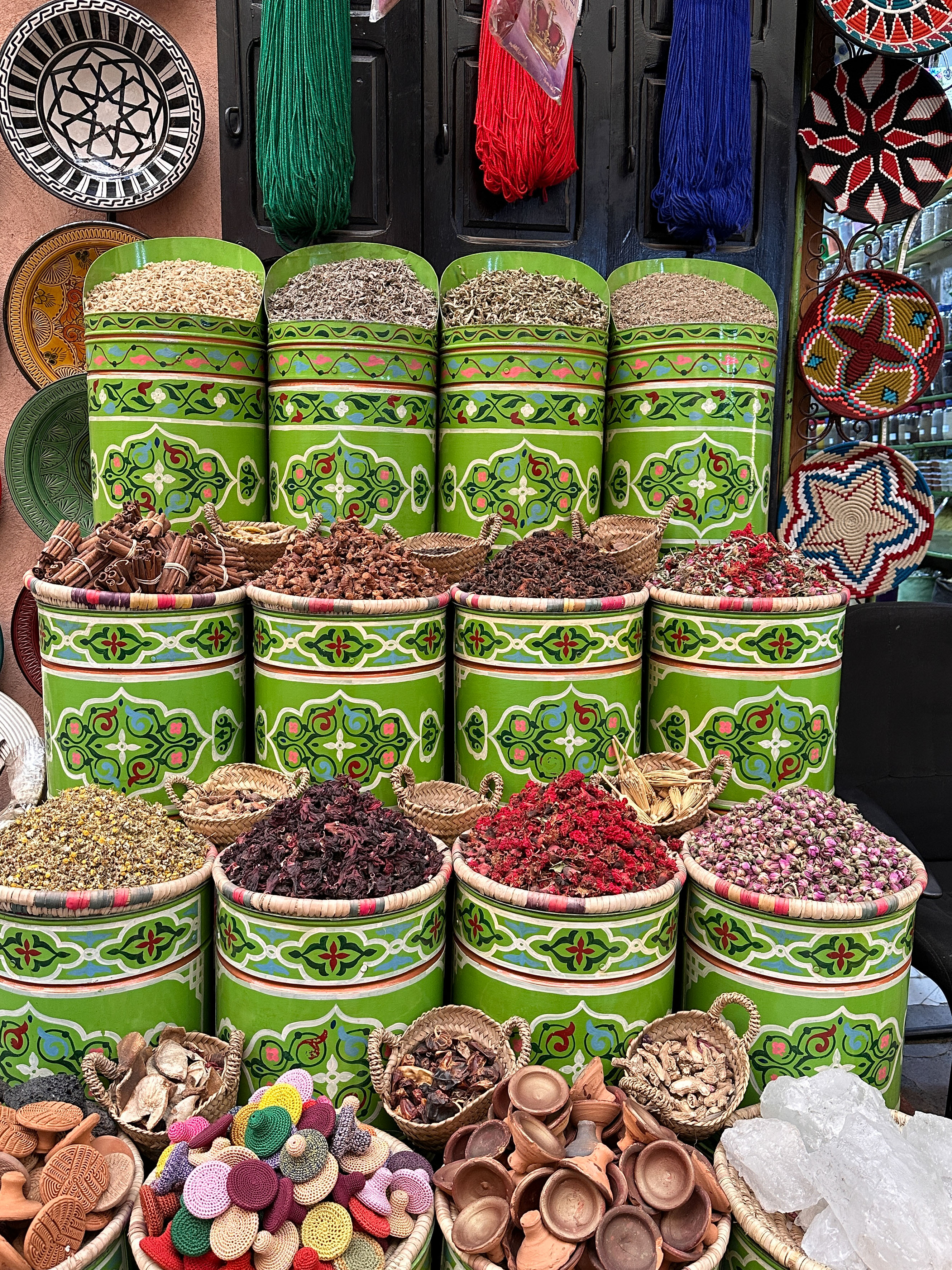 Colorful Moroccan spice market with green patterned containers of herbs & crafts.