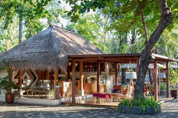 a building with a thatched roof and tables and chairs under trees