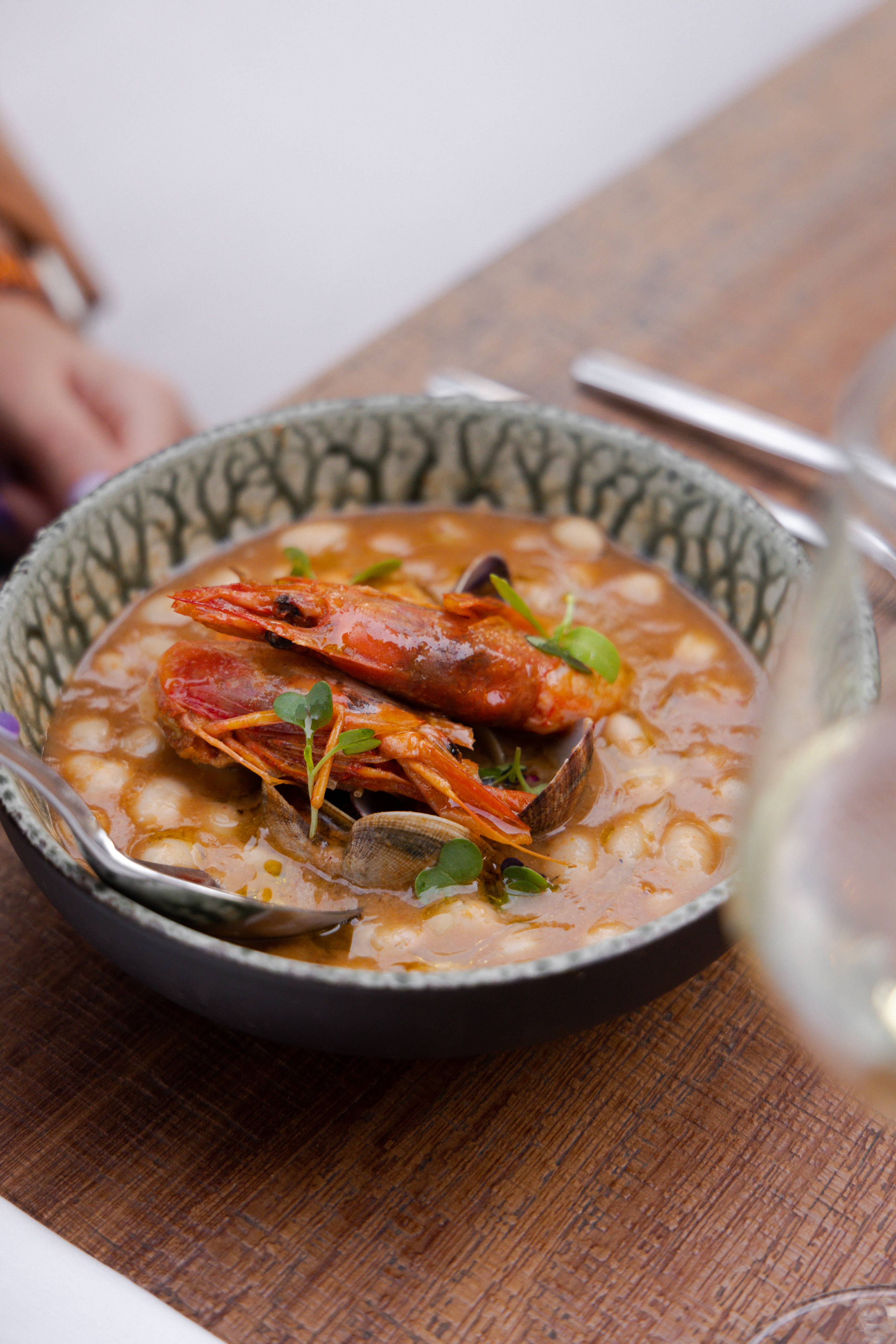 Seafood stew with prawns, clams, white beans, and herbs on a wooden table.