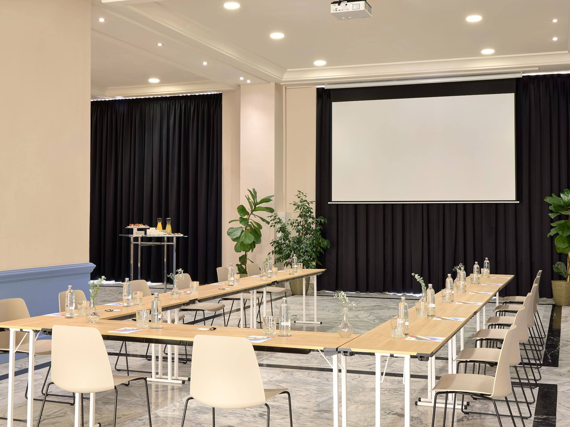 Sala de conferencias moderna con mesa en U, proyector y bebidas.