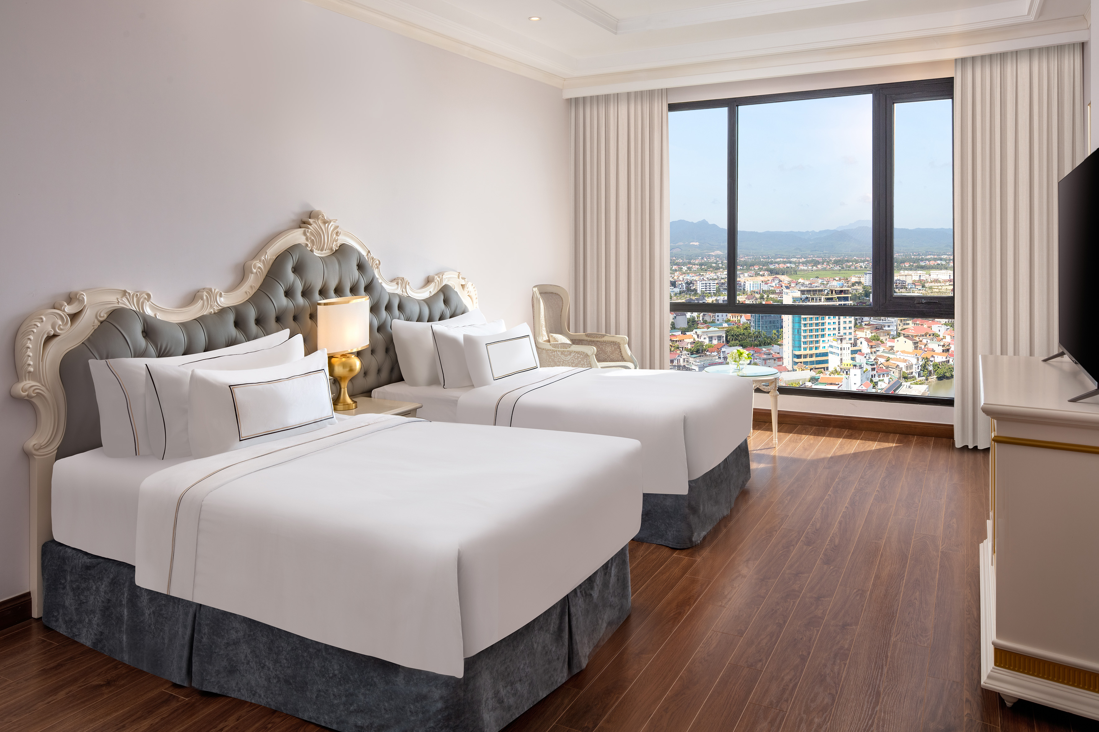 Elegant hotel room with two beds, ornate headboards, and city view window.