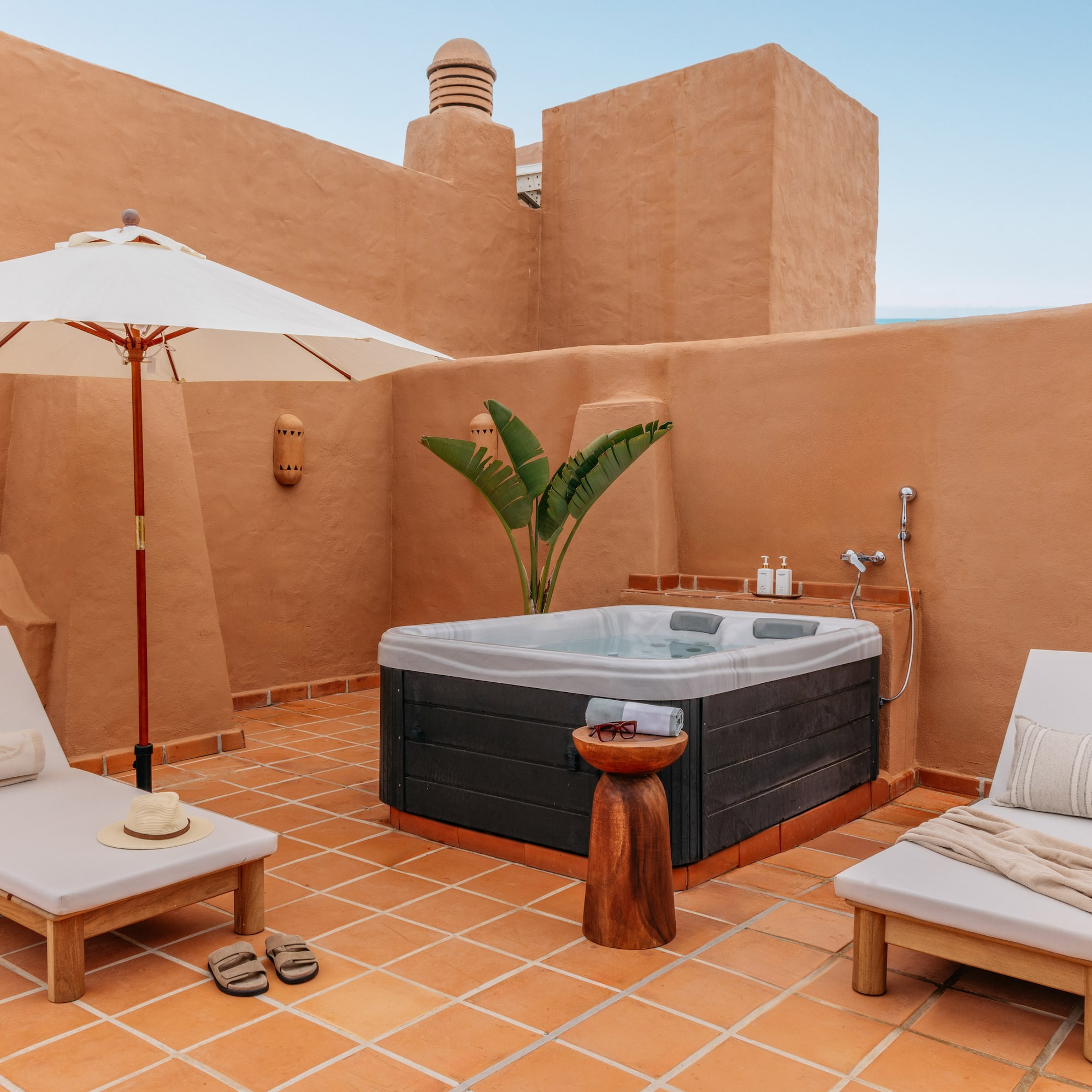 Private terracotta rooftop patio featuring hot tub, lounge chairs, and umbrella.