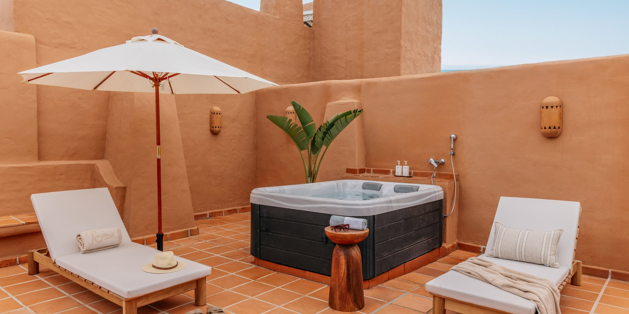 Private terracotta rooftop patio featuring hot tub, lounge chairs, and umbrella.