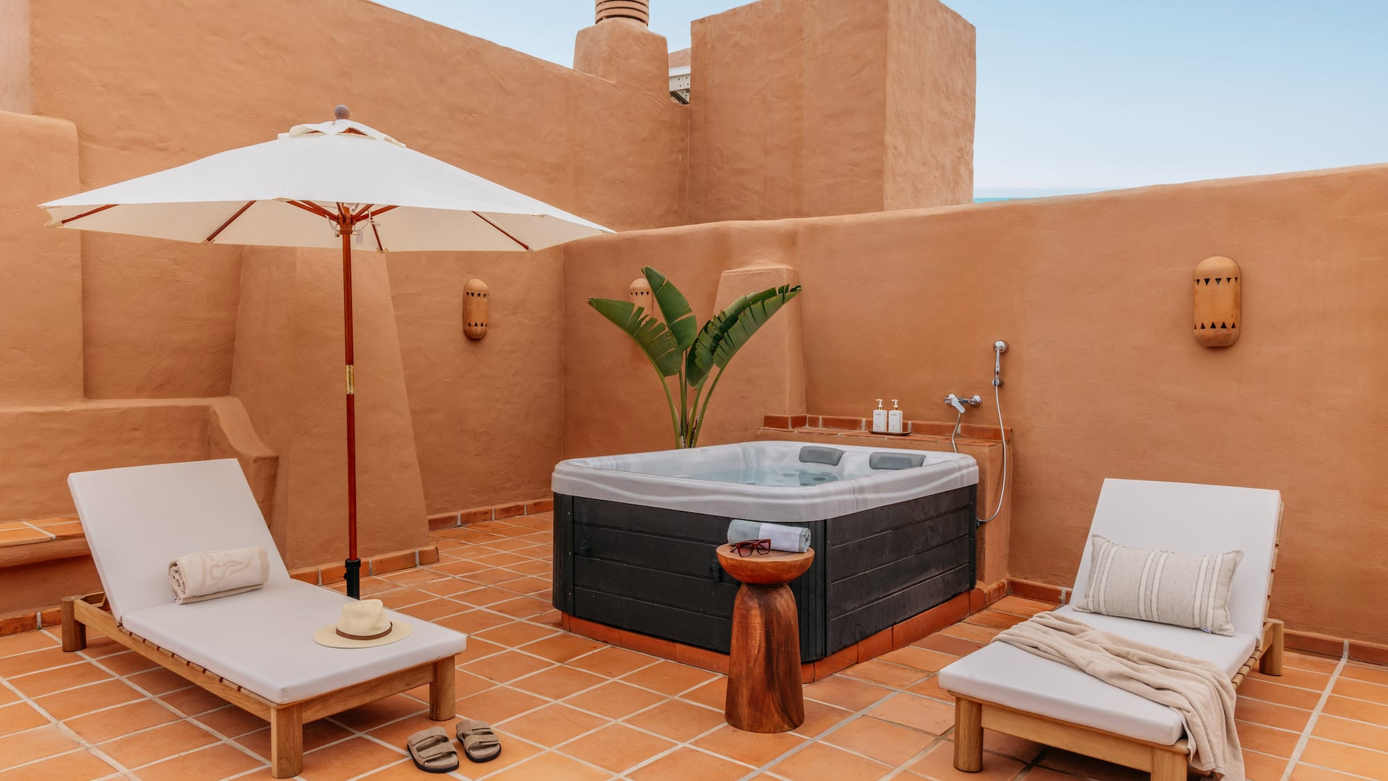 Private terracotta rooftop patio featuring hot tub, lounge chairs, and umbrella.