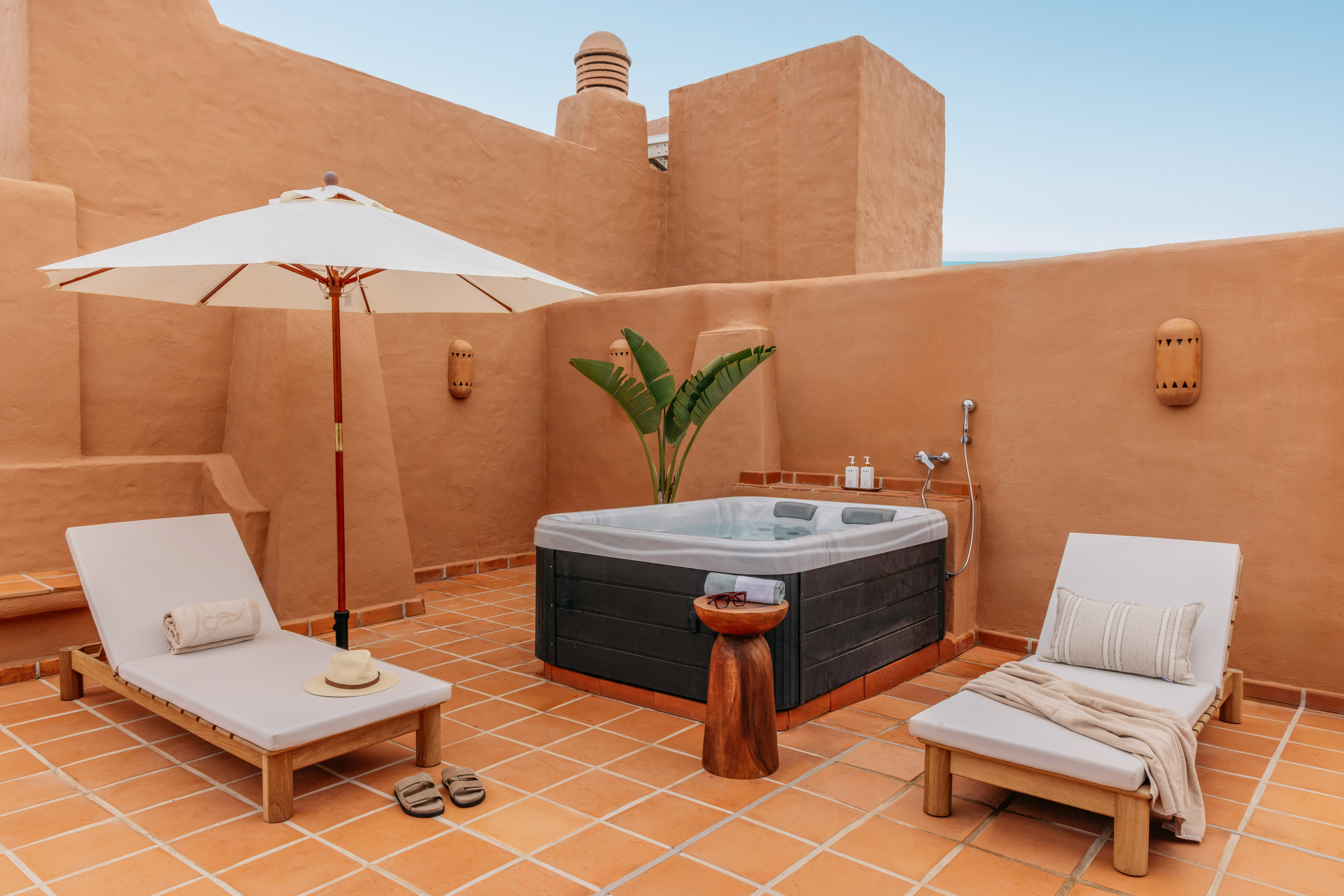 Private terracotta rooftop patio featuring hot tub, lounge chairs, and umbrella.